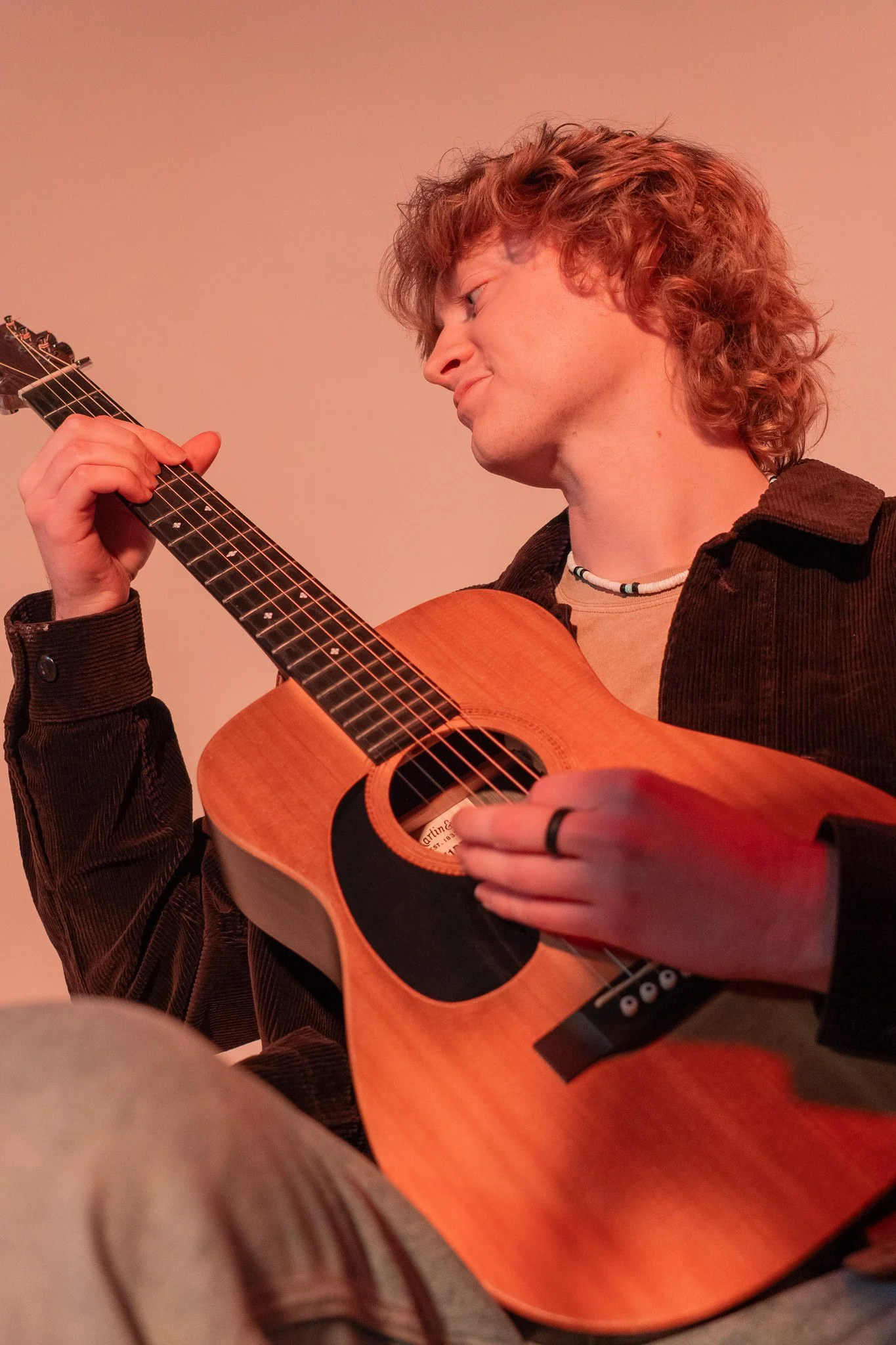 A young man playing an acoustic guitar, focusing on his side profile and the guitar.