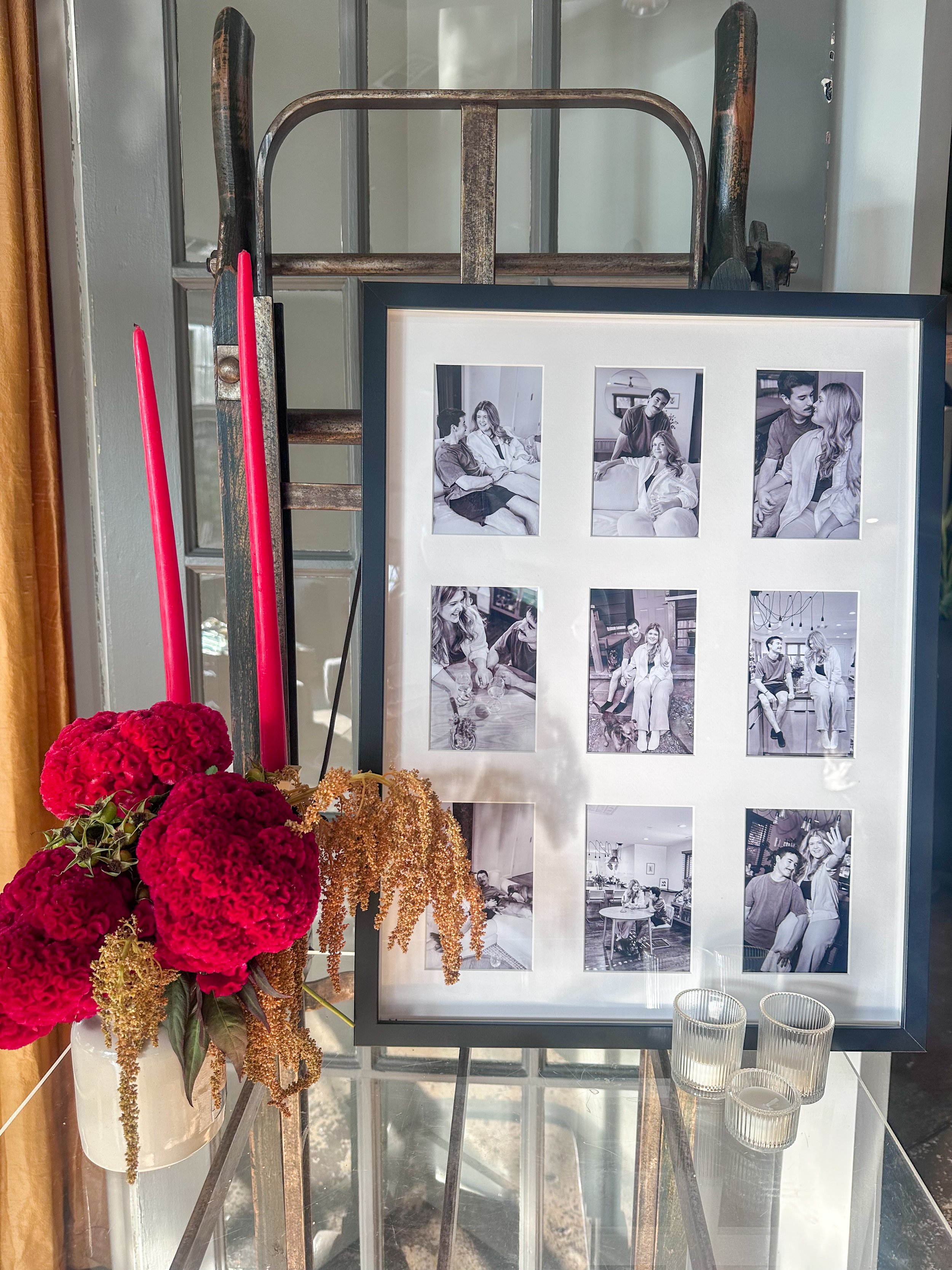 A framed photo collage displaying nine black-and-white pictures of two people, with a bouquet of red flowers and three small glass candle holders in front.