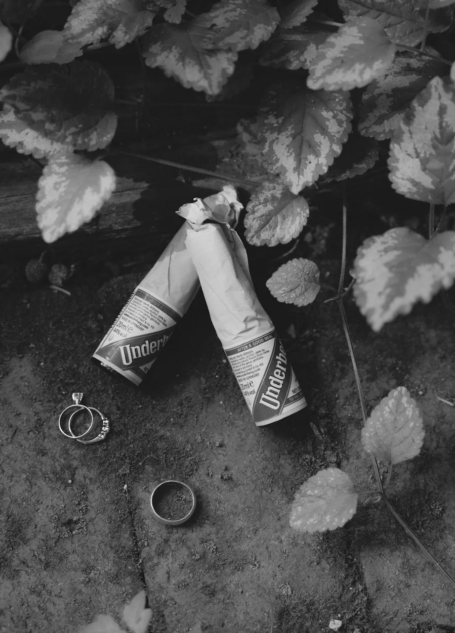 Two crumpled toothpaste tubes and two rings lying on the ground amidst large leaves.