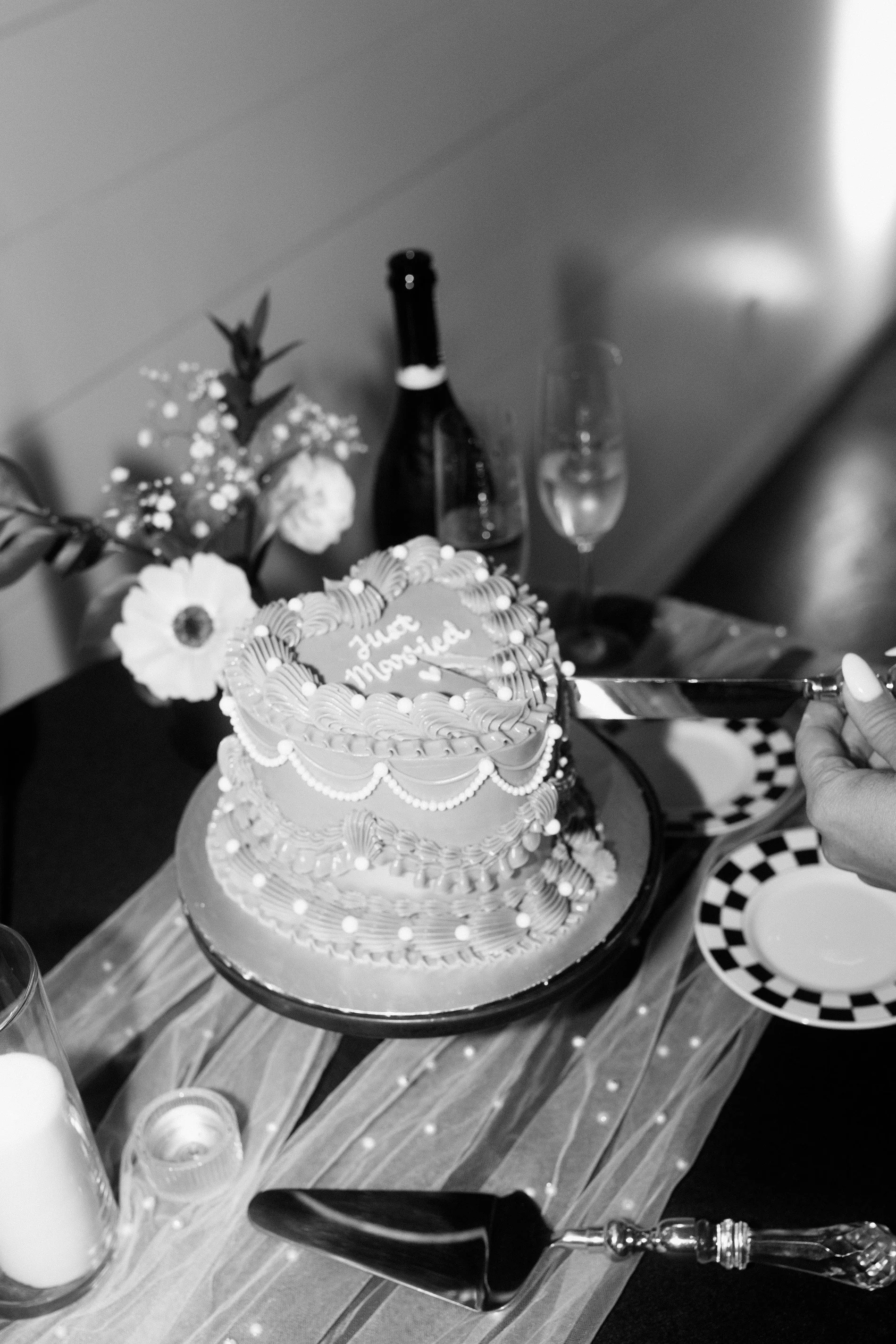 A heart-shaped wedding cake with decorated icing and the words "Just Married" written on top, placed on a table with flowers, champagne, and plates.