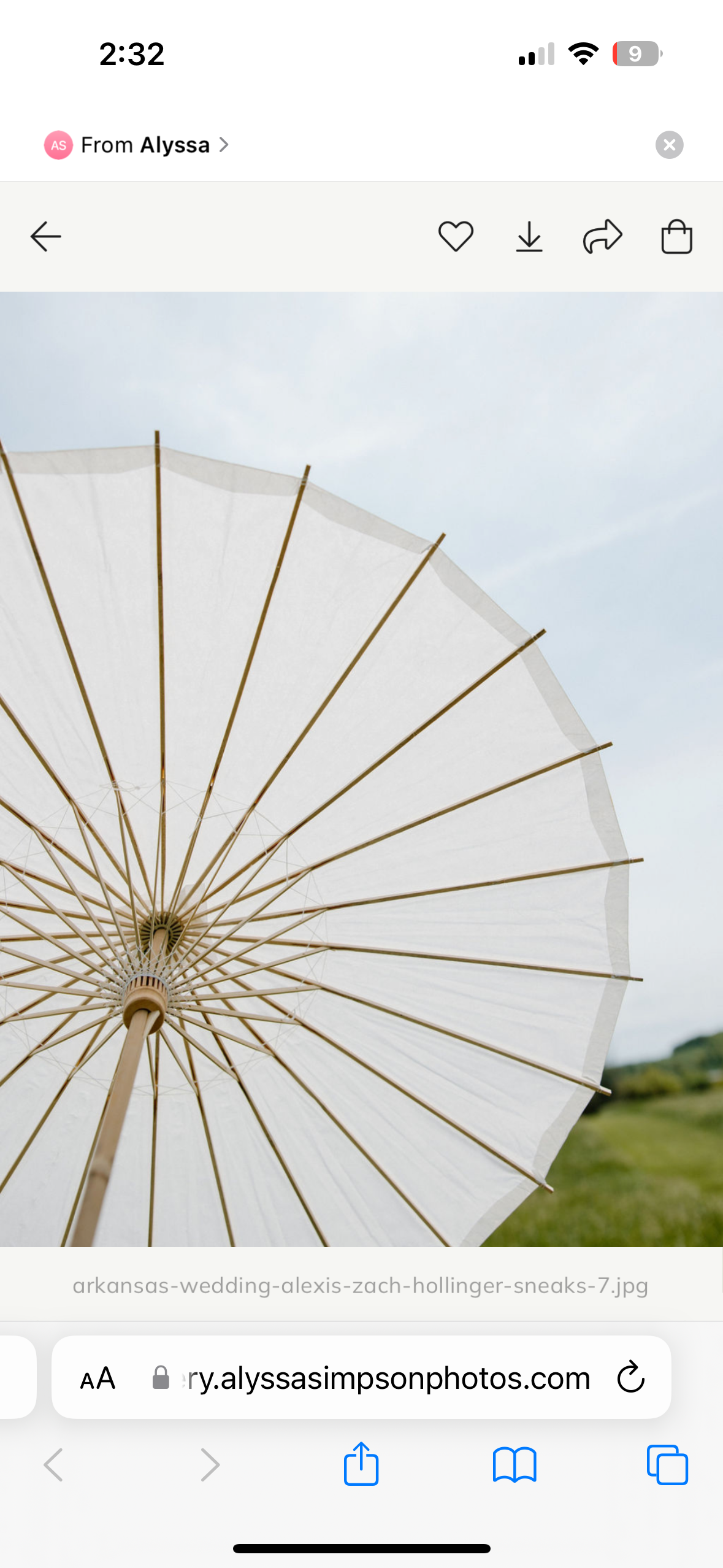 An open white parasol held up outdoors on a partly cloudy day with green trees and grass in the background.