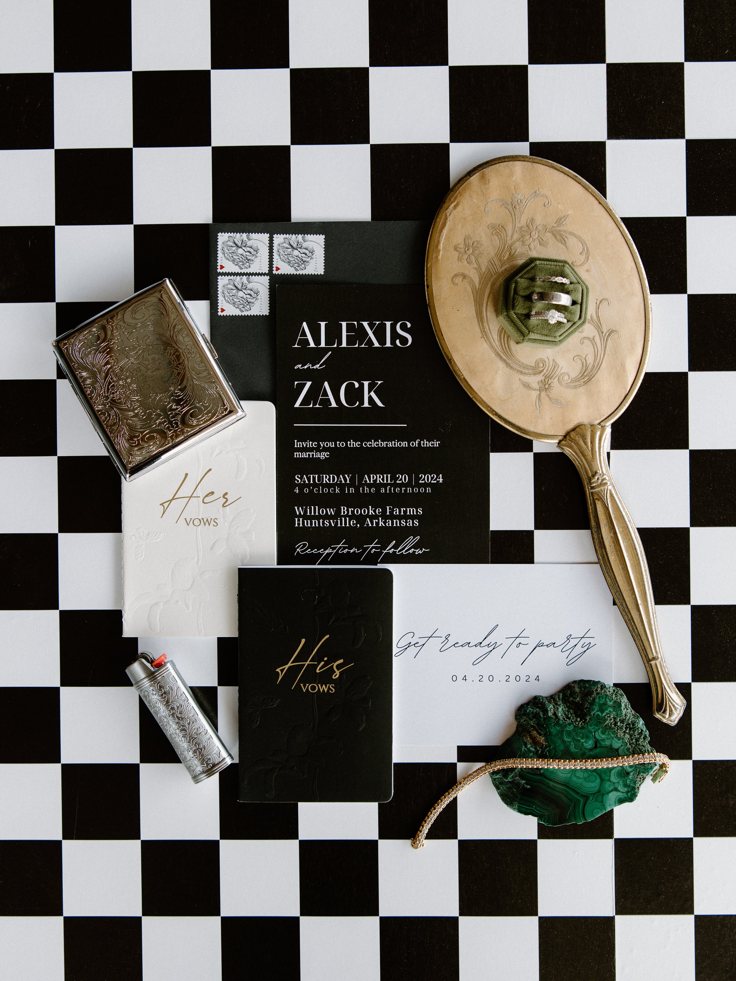 Wedding invitation suite with rings, jewelry, and accessories on a black and white checkered surface.