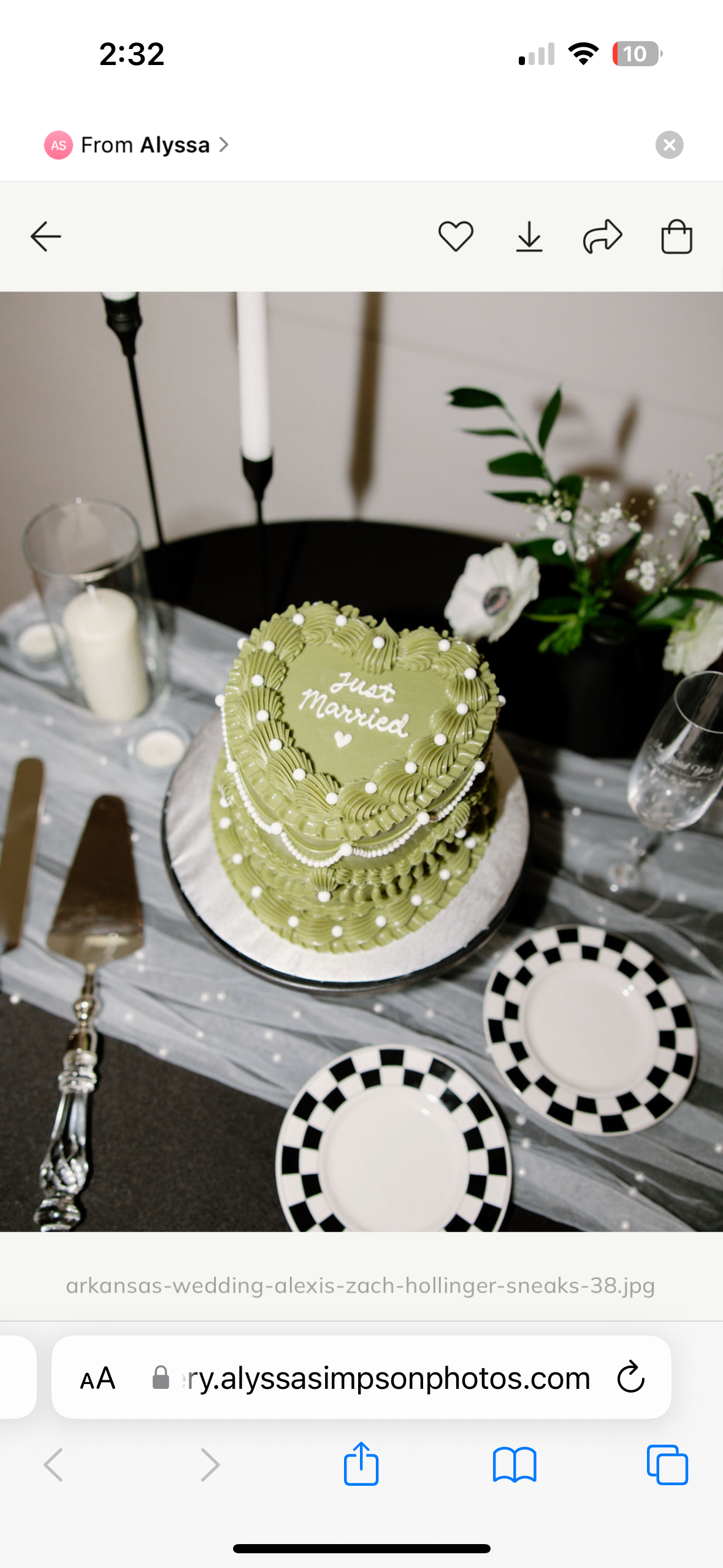 Heart-shaped green wedding cake with white and gold accents, decorated with small white balls, with 'Just Married' written on top, surrounded by candles, glasses, plates, and floral arrangements.