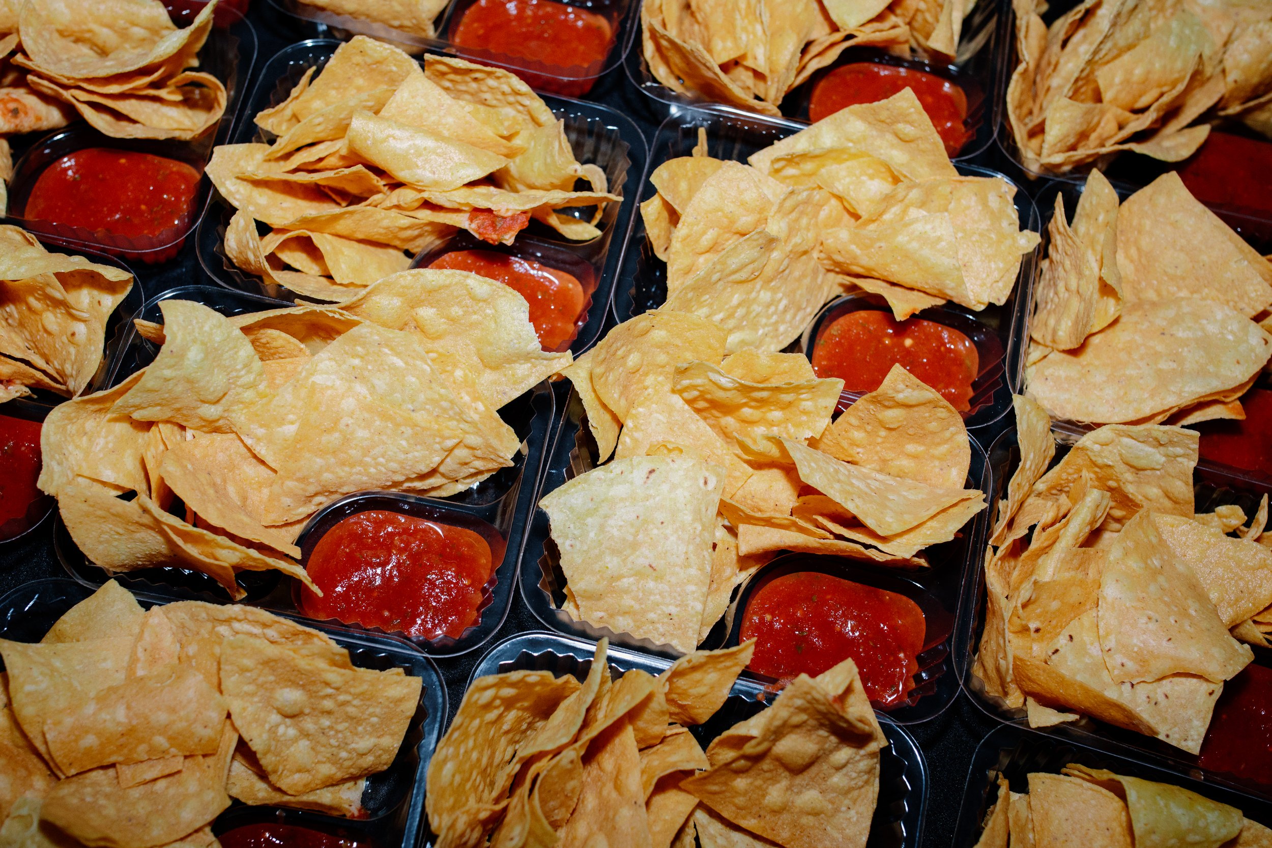 Multiple small containers filled with tortilla chips and red salsa.
