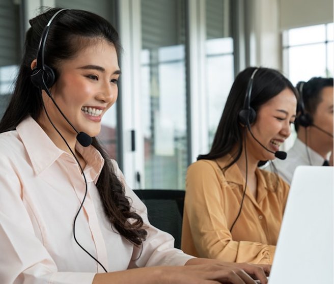 Customer service representatives with headsets working at computers in an office.