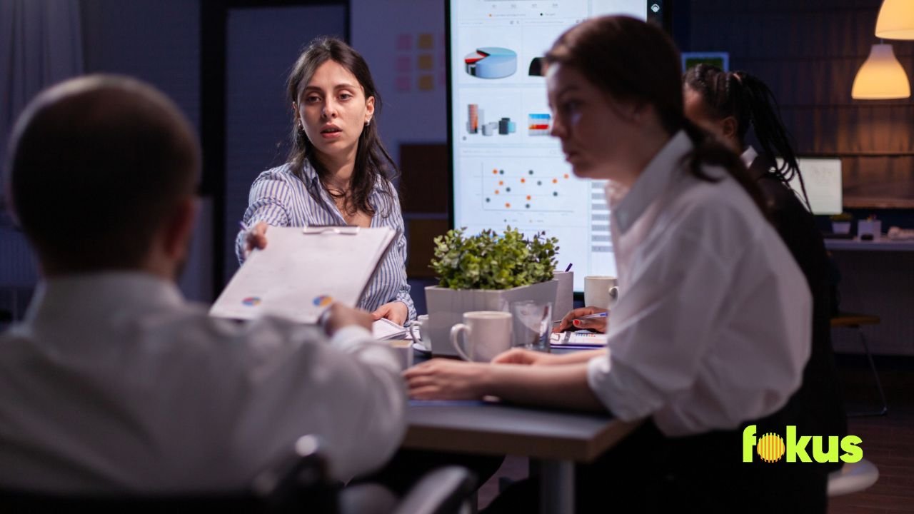 A woman giving her assessment to a man at a table, discussing a digital questionnaire for improved self-assessments.