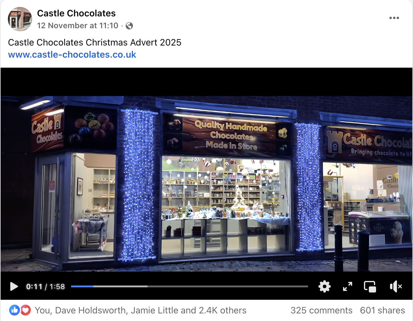 Nighttime storefront of Castle Chocolates decorated with blue string lights, display window showing chocolates and festive decorations, and signage indicating handmade chocolates in-store.