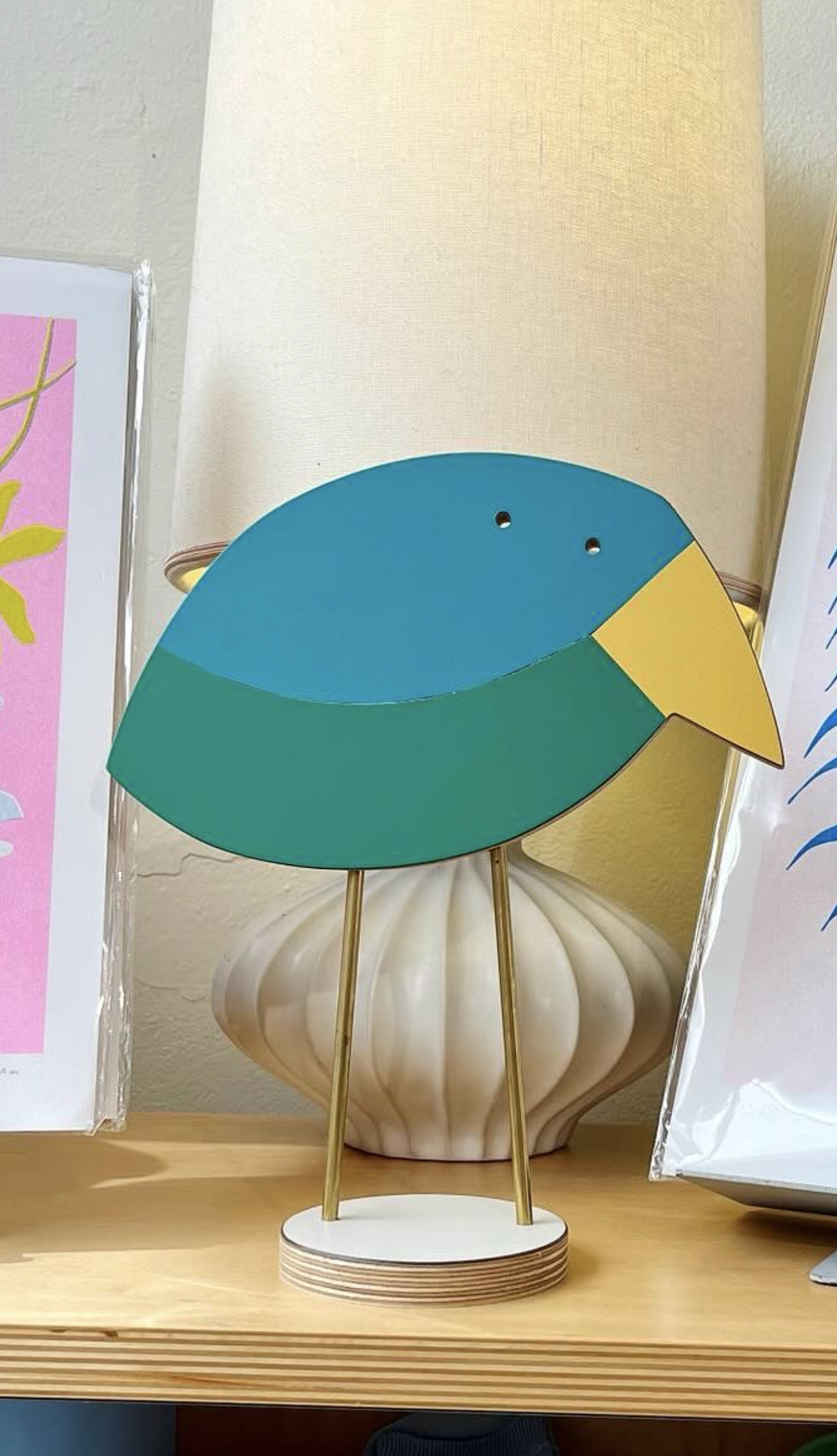 Decorative bird sculpture with a blue and green body and yellow beak on a wooden base, placed on a wooden surface.