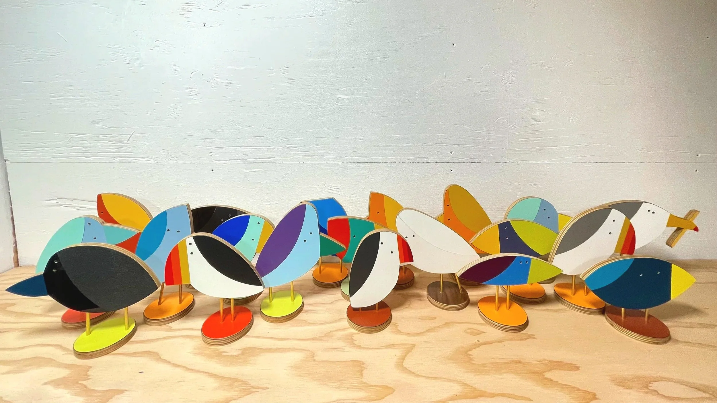 Colorful wooden bird sculptures with geometric patterns, arranged on a wooden surface against a plain white wall.