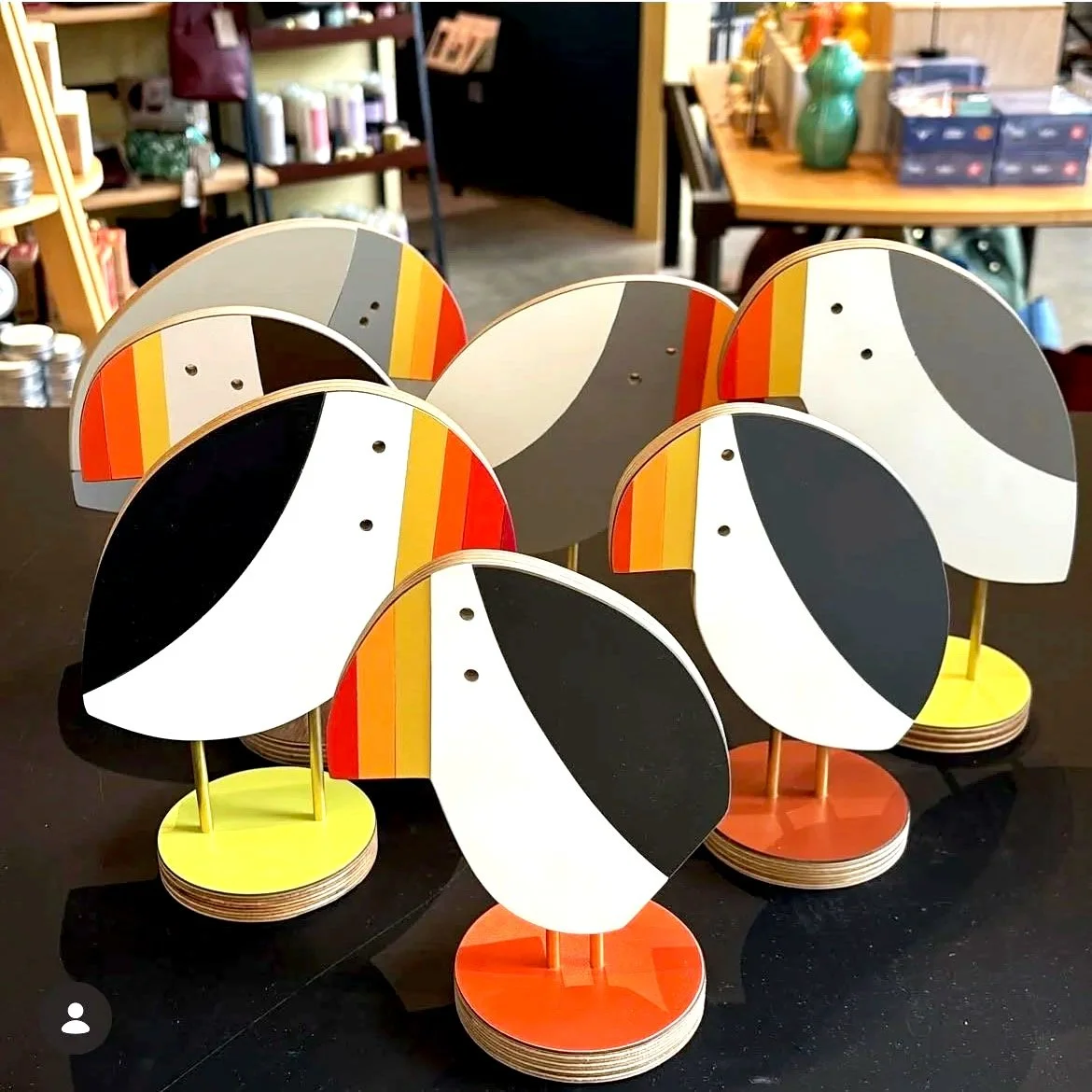 Colorful decorative objects resembling owl faces with abstract black, white, yellow, red, gray, and orange patterns arranged on a black table in a store setting.