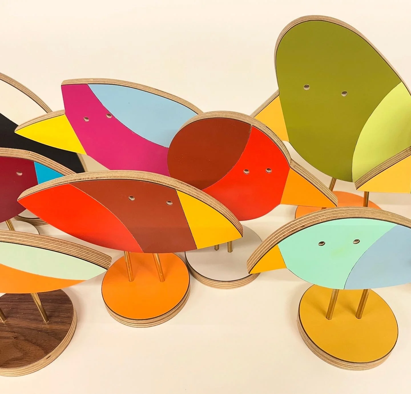 Colorful abstract wooden sculptures resembling butterfly or bird shapes with semicircular wings and circular bases.