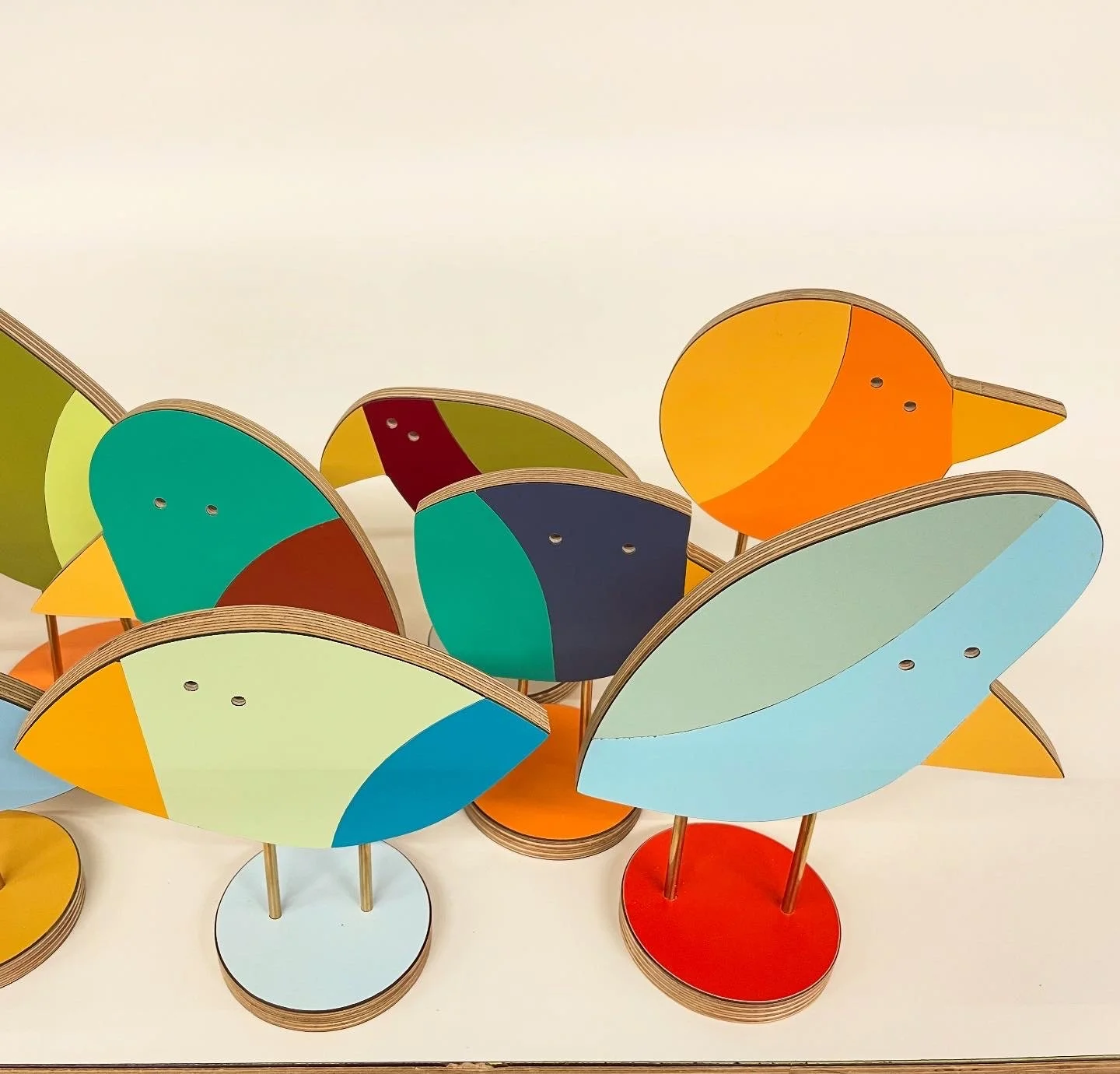 Colorful bird-shaped wooden stands with curved bodies and pointed beak designs, arranged in various positions.