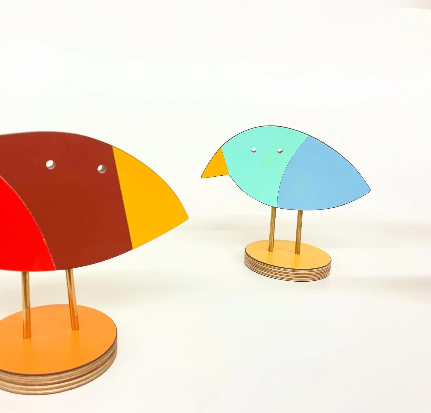 Colorful wooden bird figurines with circular bases and small round eyes, facing each other against a white background.