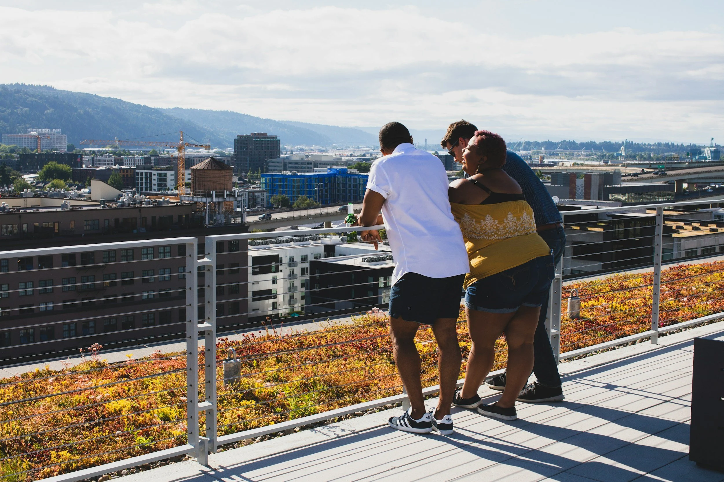 Three people standing at a railing overlooking a city view.