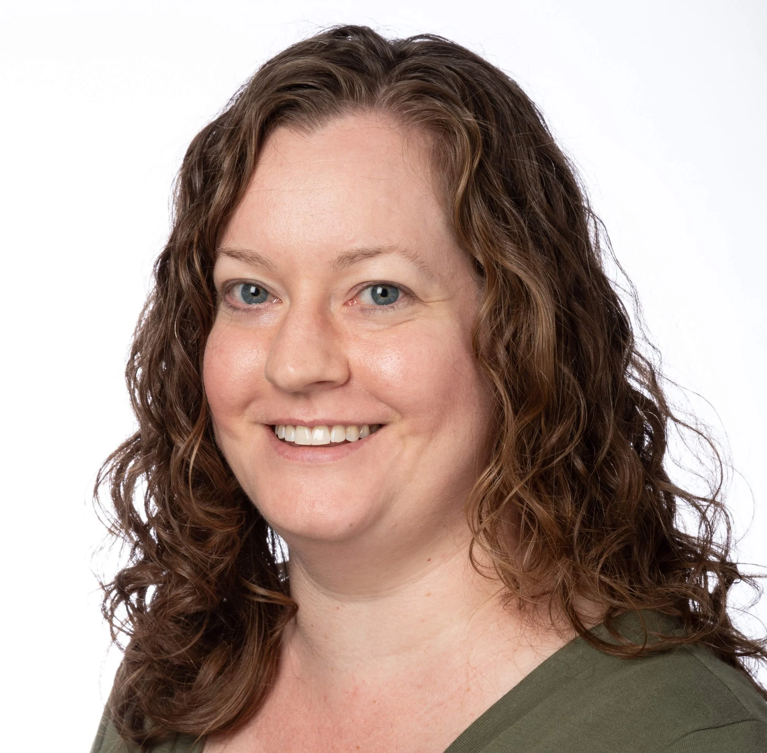 Female attorney with long curly brown hair, blue eyes, and fair skin smiling at the camera. She is wearing a green top and is set against a white background.