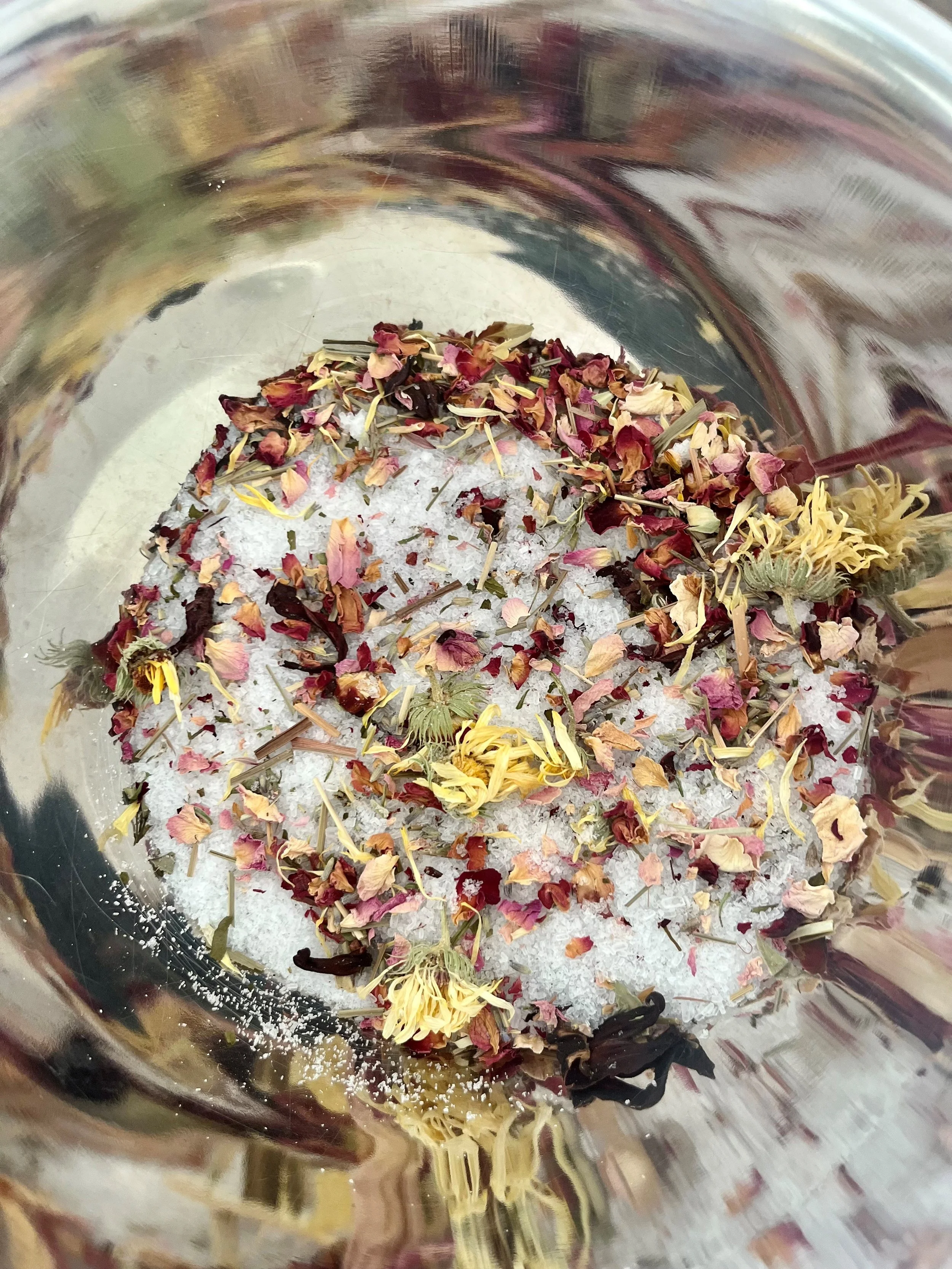 Salt with various dried herbs and flowers inside a glass container.