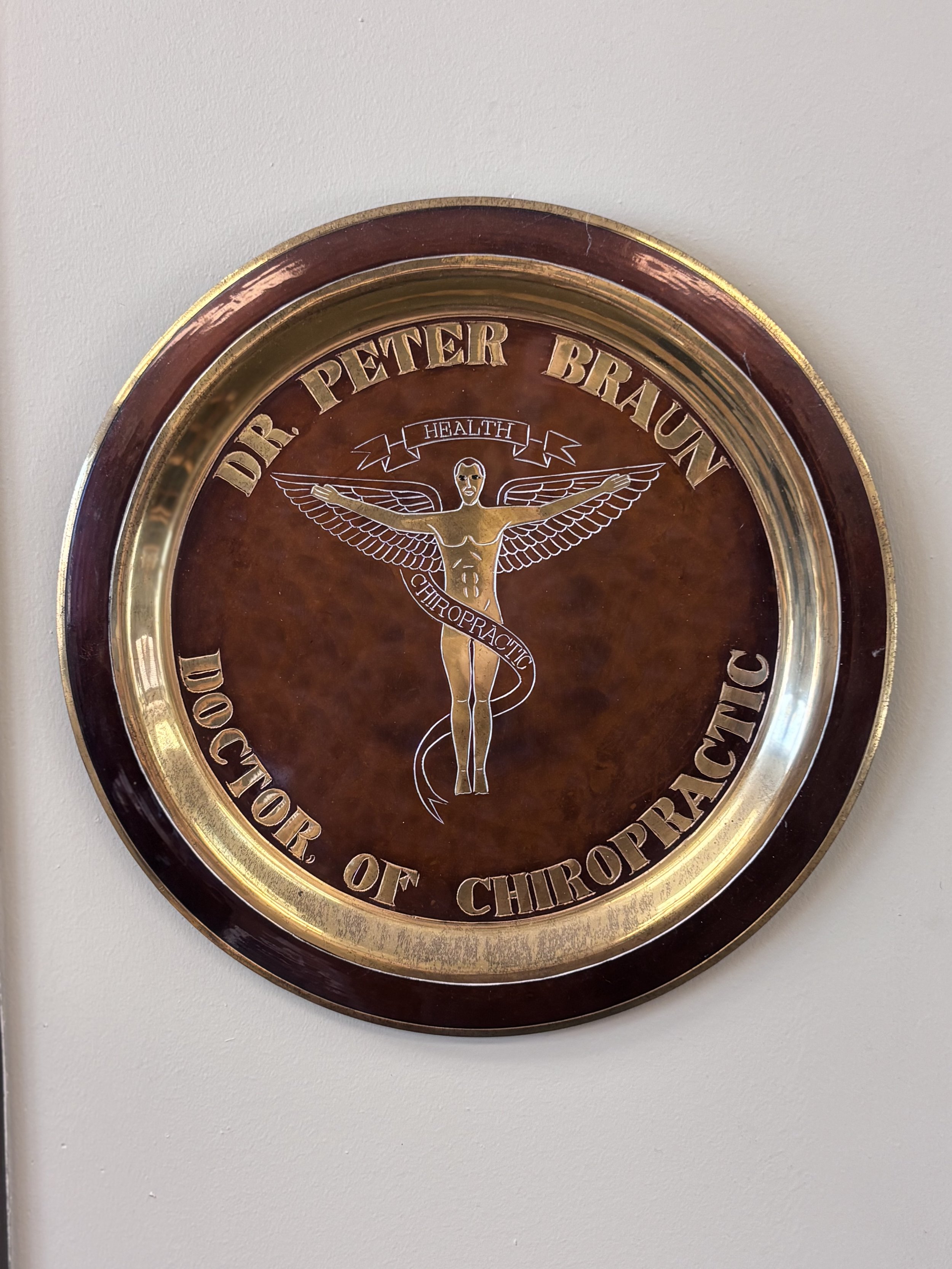 Decorative wall plaque for Dr. Peter Braun, Chiropractor, featuring a winged human figure and the words 'Health' and 'Chiropractic'.