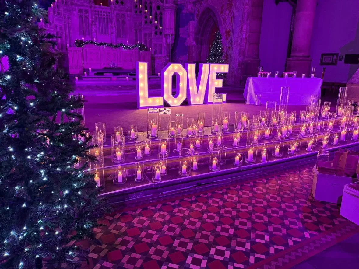 Decorated event space with large illuminated 'LOVE' sign, Christmas trees, numerous candles in glass holders, and purple lighting, in a historic building.