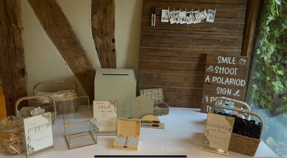A photo booth setup with photo props, sign-in sheet, and a wall display with a sign that says, 'Smile, shoot a polaroid, sign, pose, turn.'