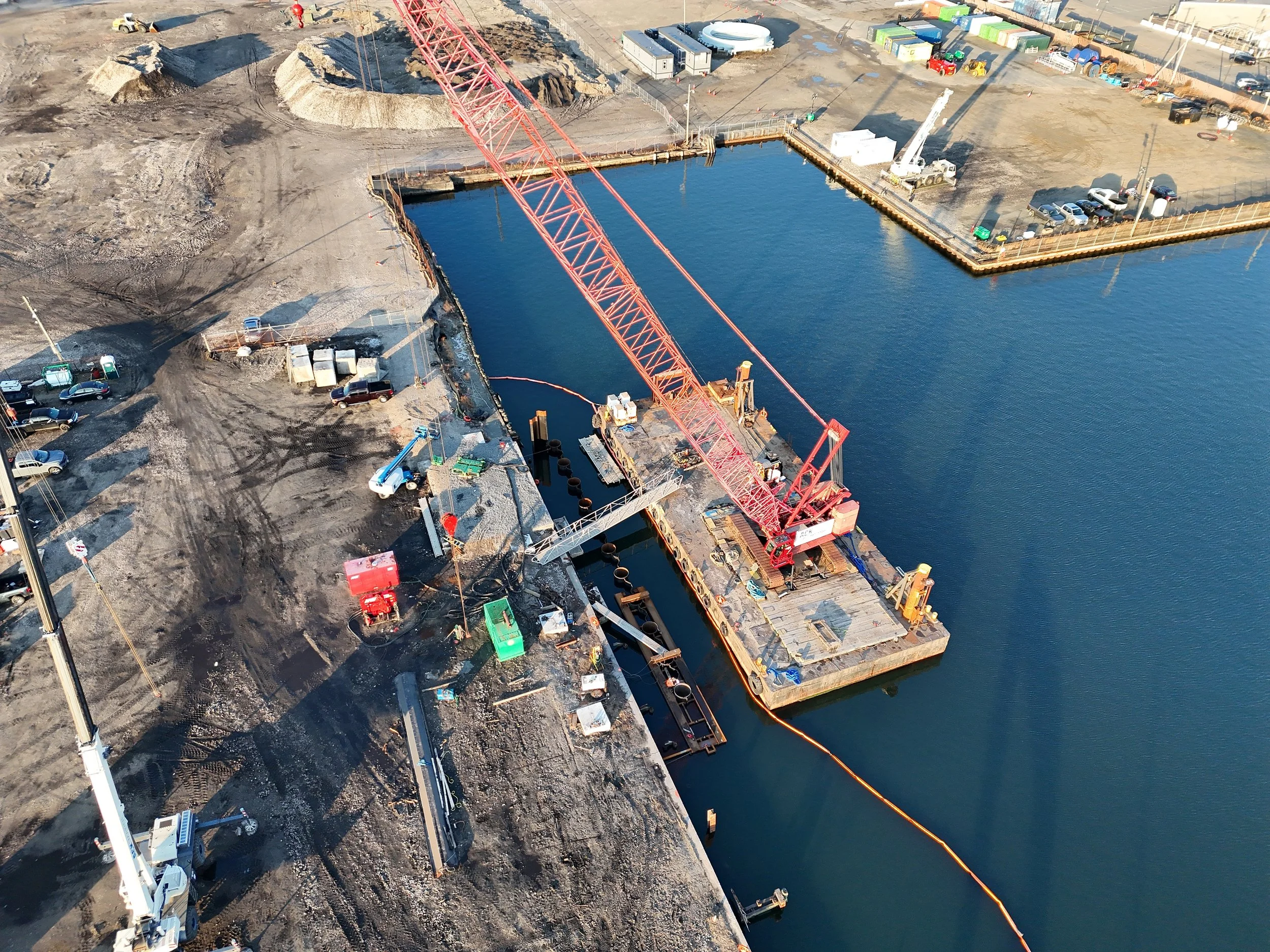 Construction site on water with a large red crane, construction vehicles, and machinery.