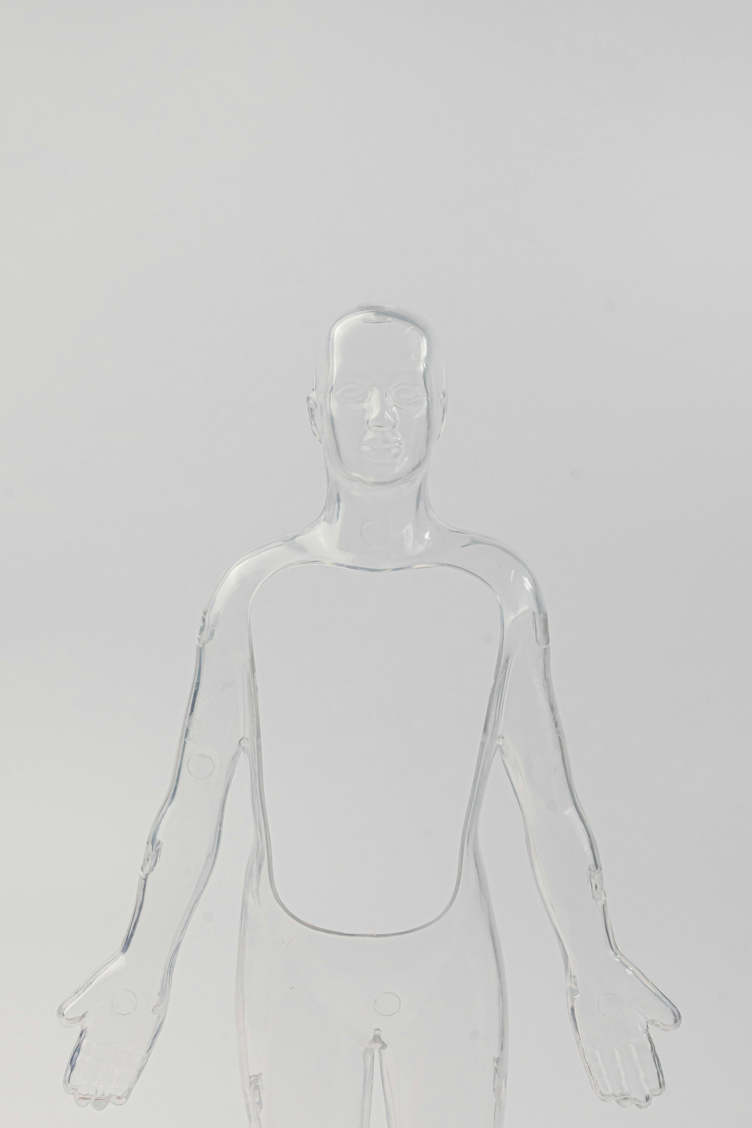 Transparent plastic mannequin outline of a human figure with arms extended downward, set against a pale background.