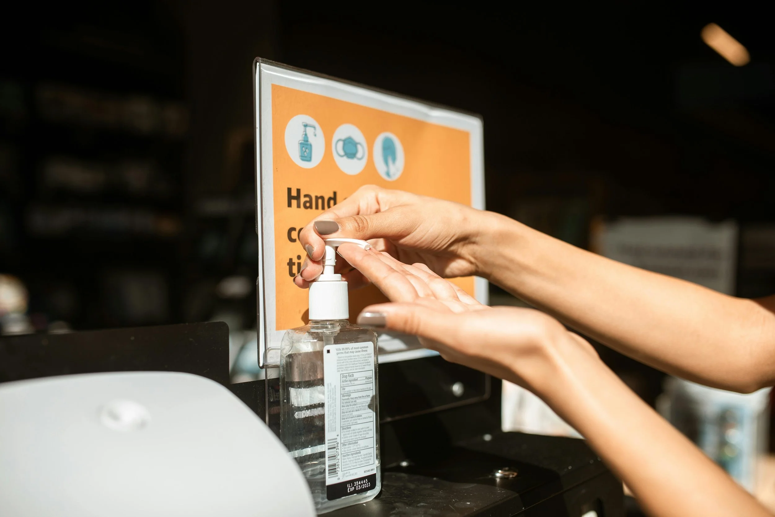A person using hand sanitizer pump dispenser in front of a sign with hand hygiene instructions.