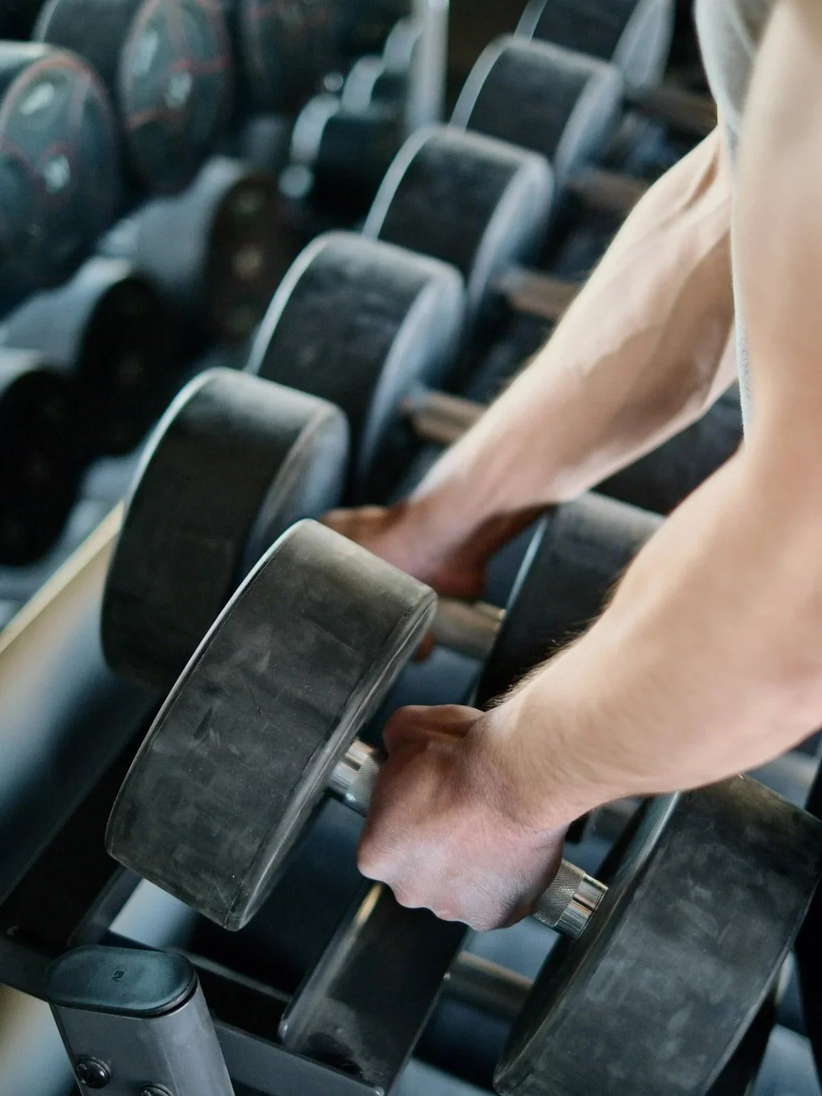 Close-up of a person lifting a dumbbell in a gym, with several other dumbbells lined up on a rack.