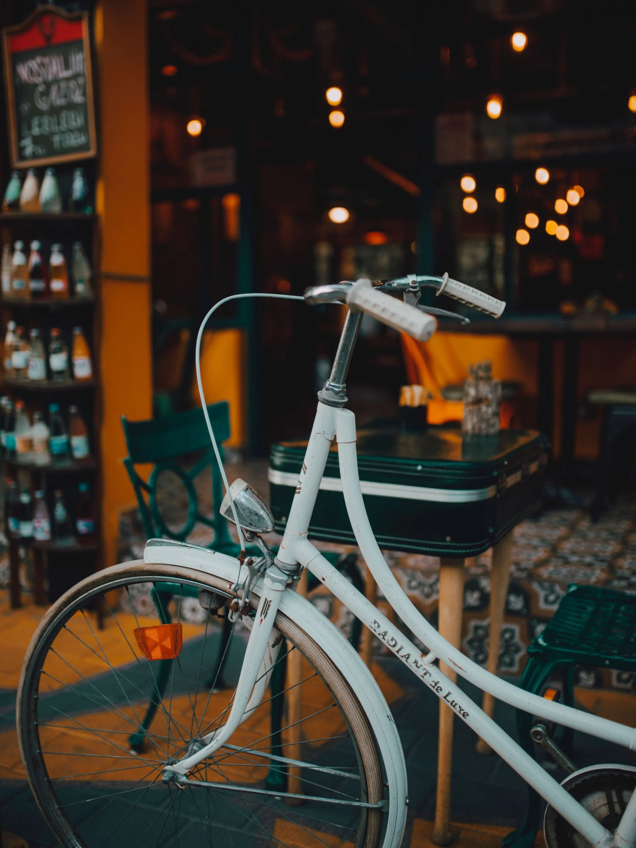 White bicycle with rust on the frame in a cozy indoor cafe setting with warm lighting, table, and chairs.