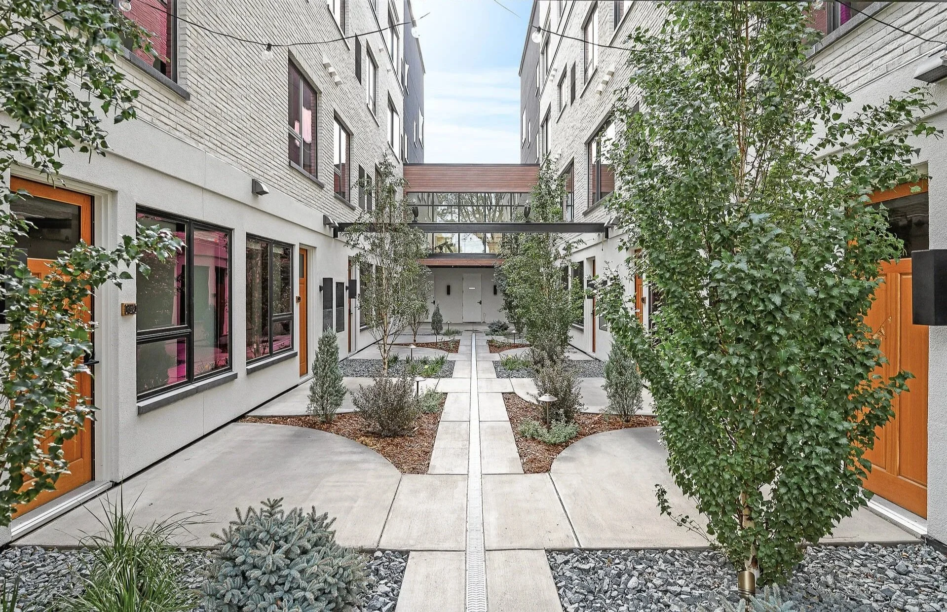 Modern apartment building courtyard with symmetrical landscaping, trees, and walkways.