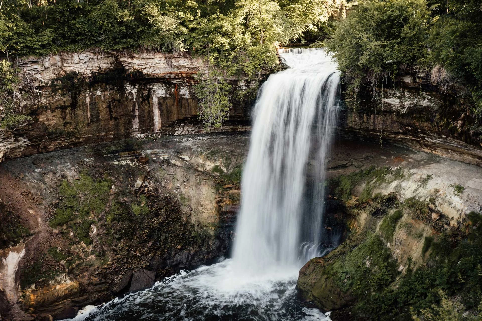 A waterfall cascading over rocks surrounded by lush green trees.