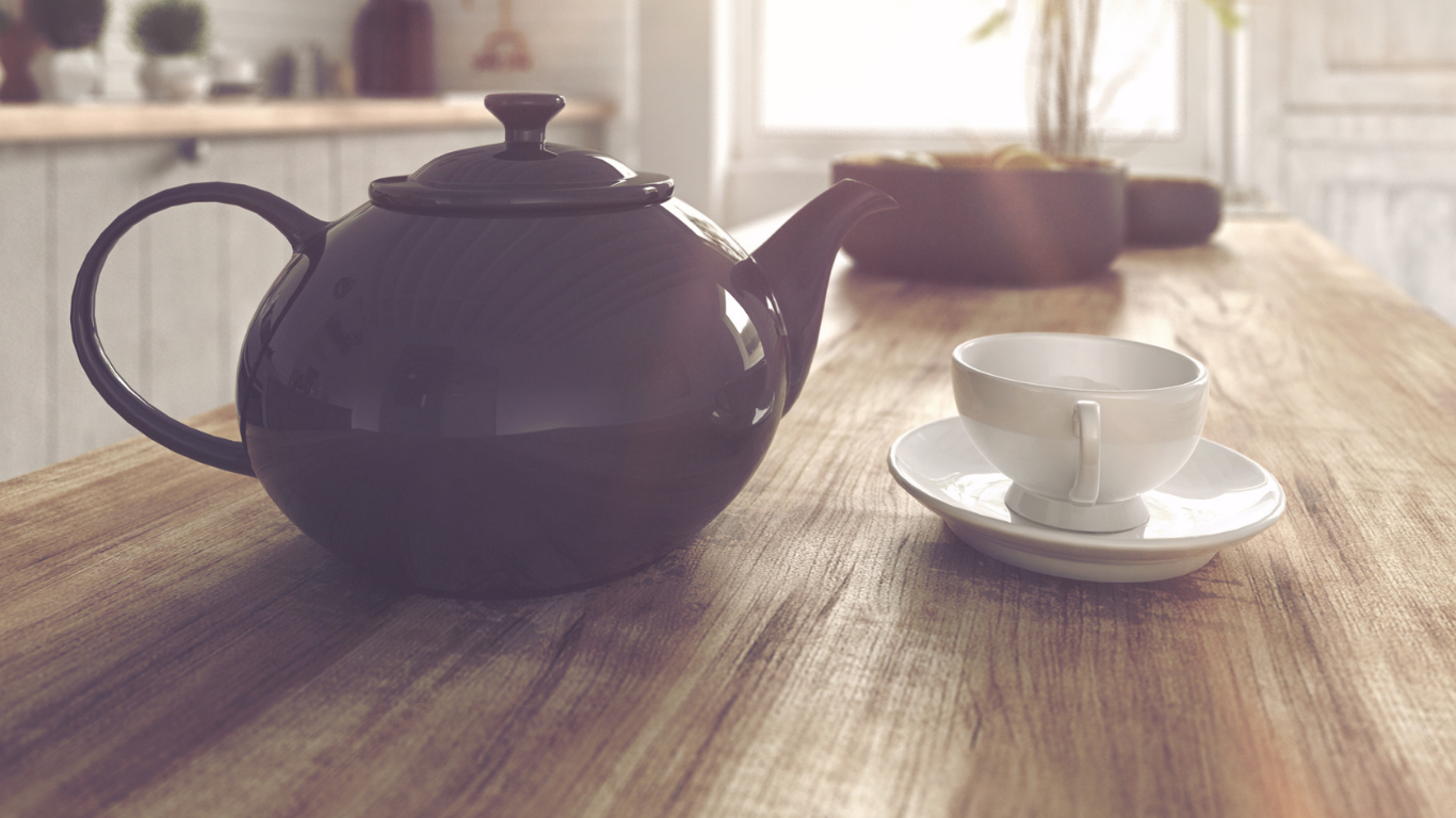A black teapot and a white teacup with a matching saucer on a wooden table in a bright kitchen.