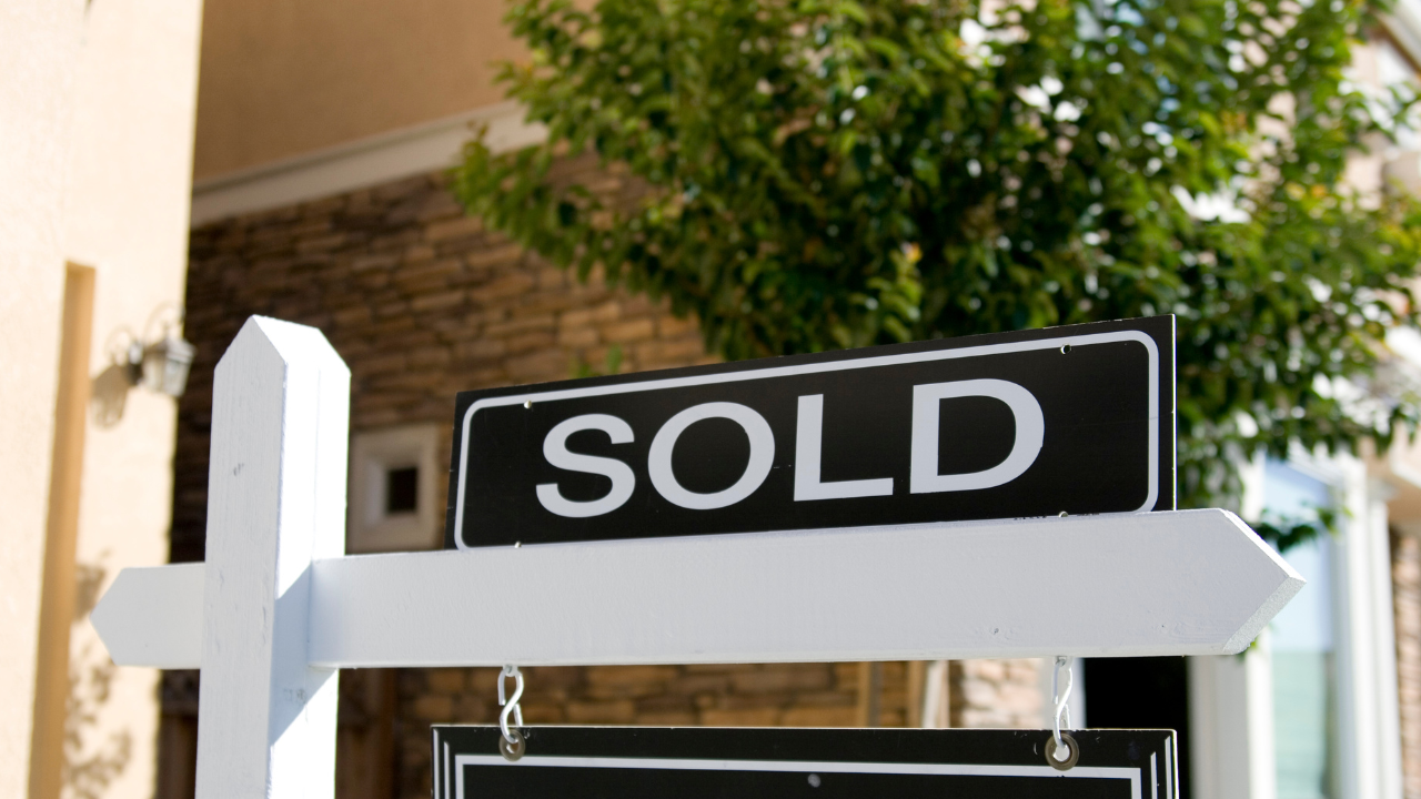 A street sign with a black background and white text that says 'SOLD', mounted on a white post.