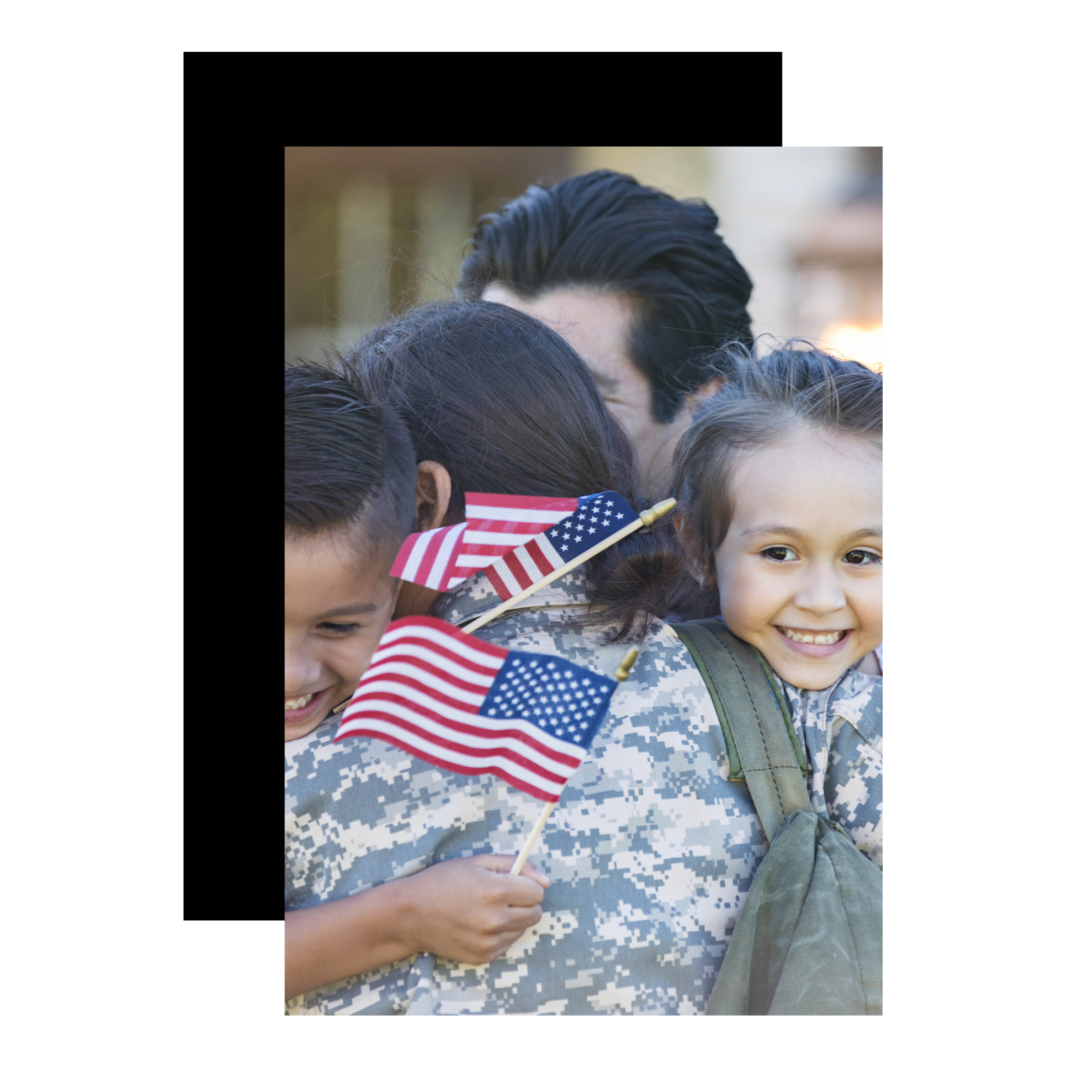 A soldier in military uniform holding children, some holding American flags, in a group hug.