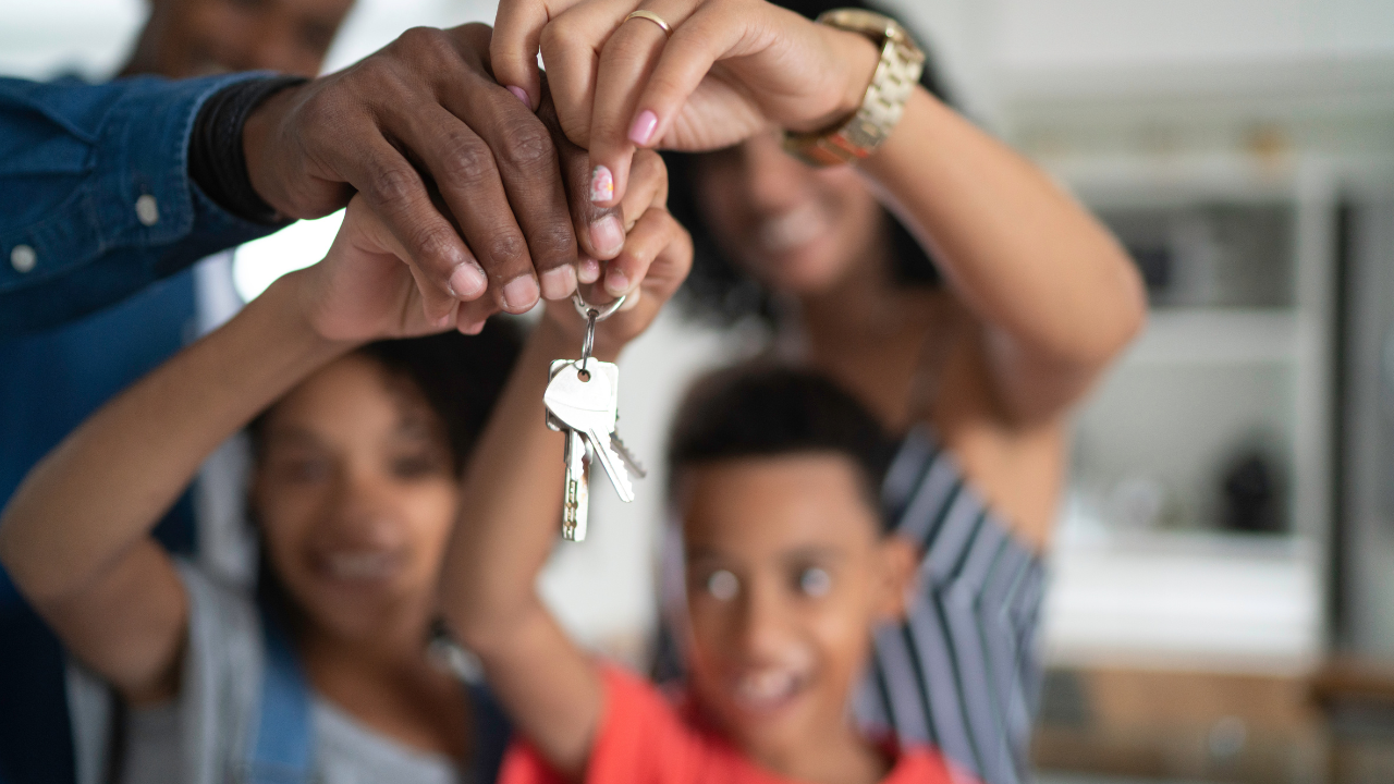 Family holding a set of keys in the air, smiling, with a kitchen background.