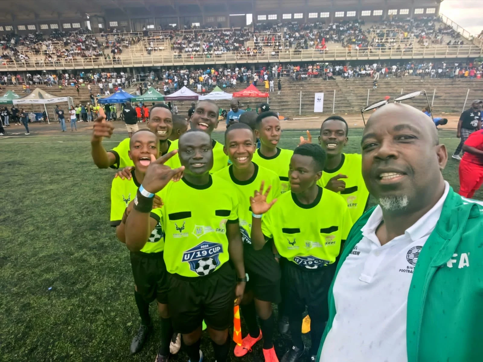 A group of football referees in bright yellow jerseys smling on a soccer field.