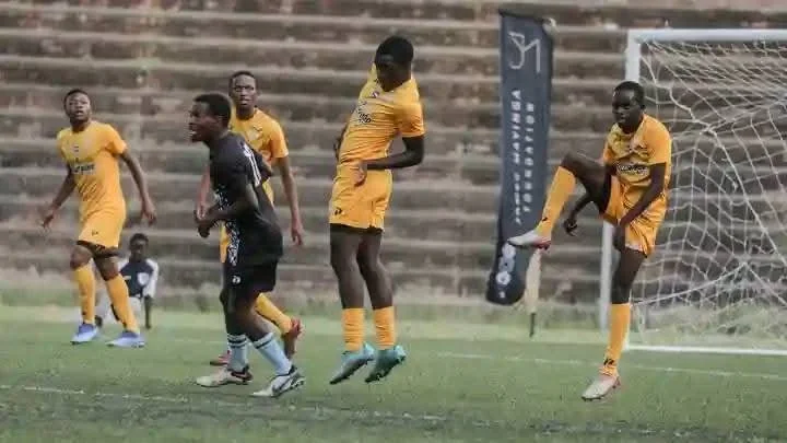 Soccer players in black and yellow jerseys on a field, some jumping, near goalpost during a game.
