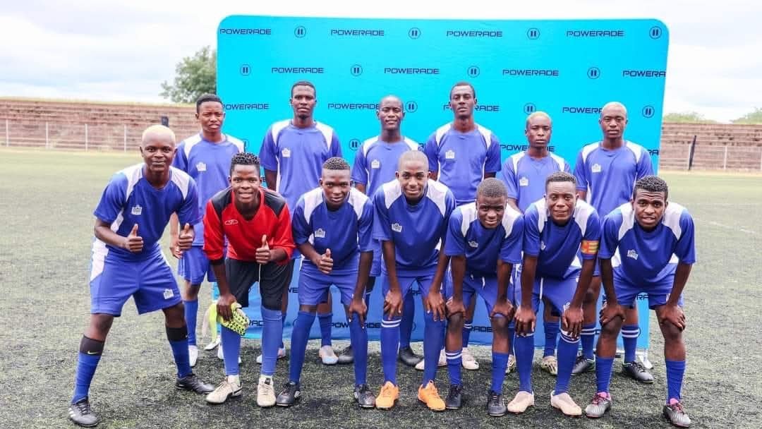 A group of 11 young male soccer players in blue uniforms posing on a soccer field with a blue backdrop that has Powerade branding.