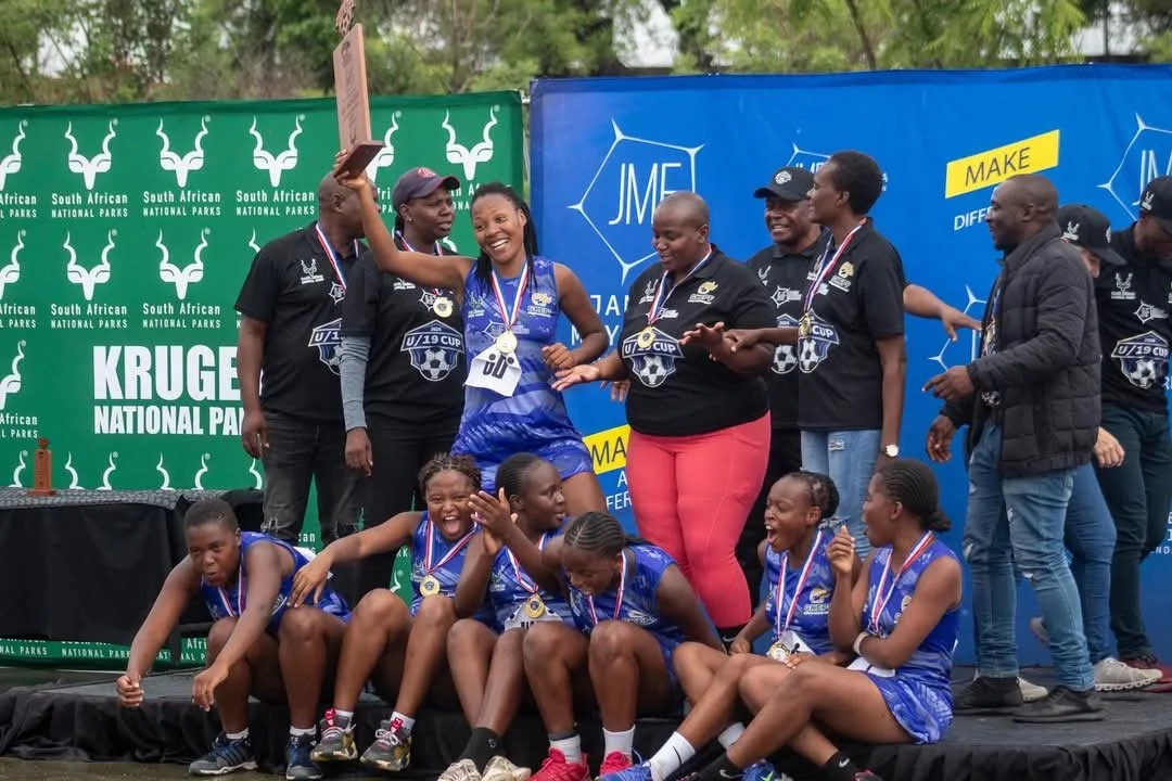 Group of young female athletes in blue uniforms with medals, celebrating on a stage.