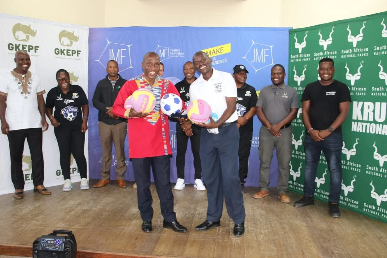 Group of people standing on a stage, some holding donated shoes, with banners of South African National Parks, GKEPF and James Mayinga Foundation in the background.