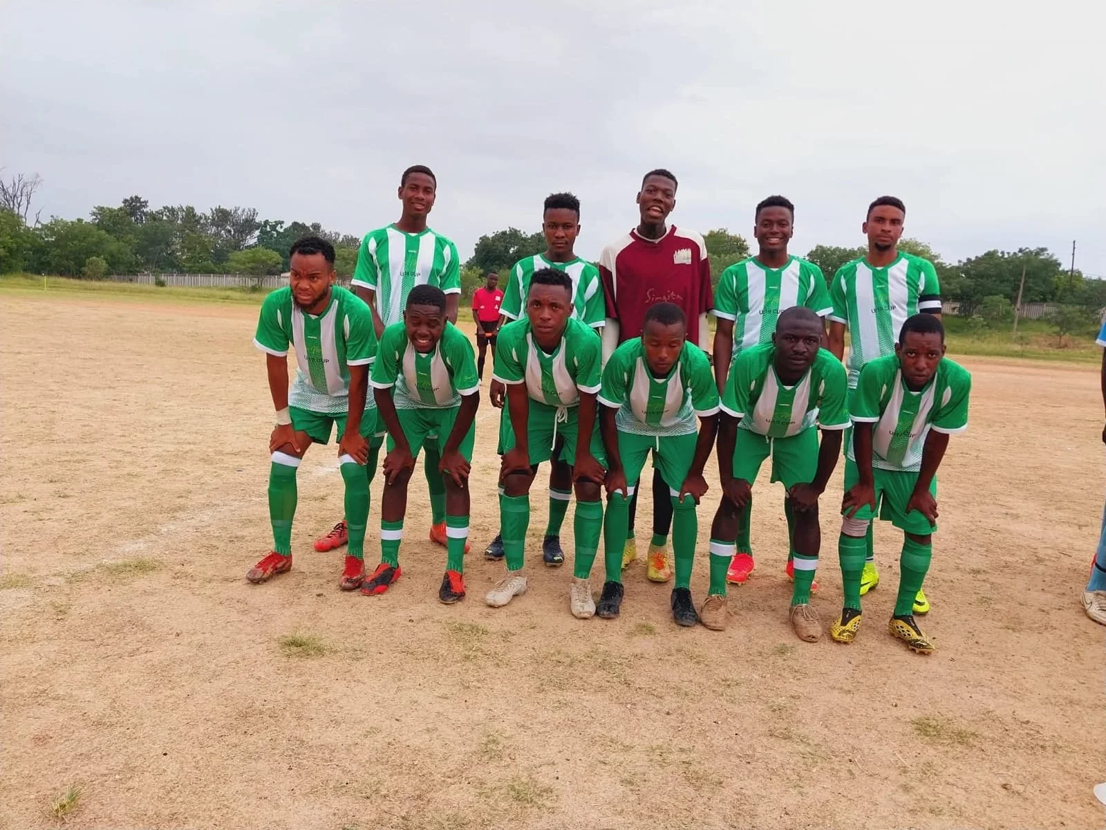 A group of eleven soccer players dressed in green and white uniforms posing on a dirt field.