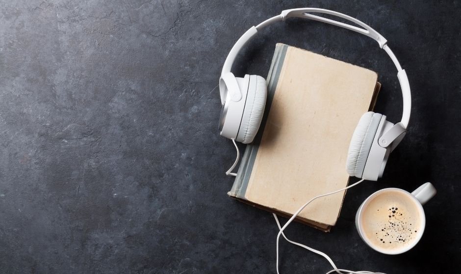 Book on dark gray surface with headphones around it and coffee next to it. Image for Book Architect Level 4 Publishing Package.