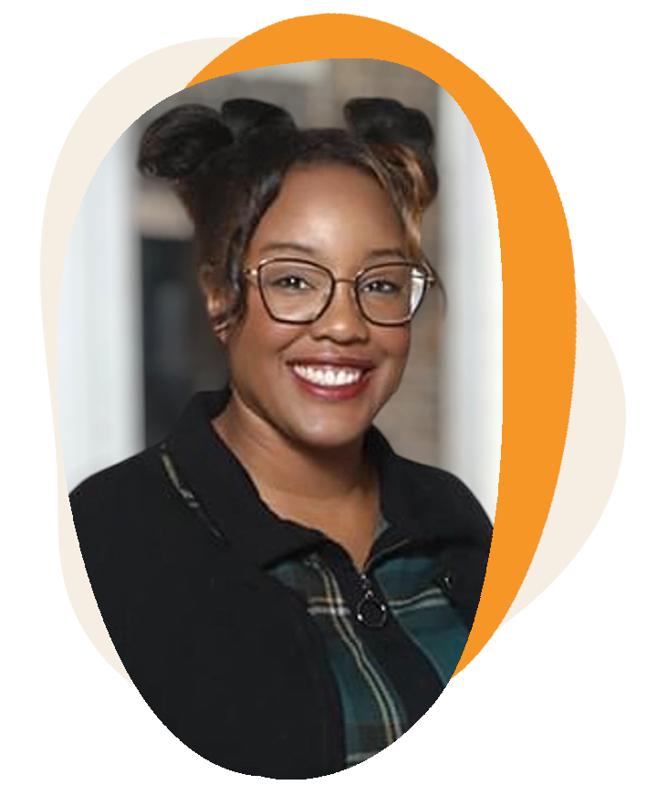 A young woman with glasses, smiling, with her hair styled in two buns, wearing a black and plaid zip-up jacket, in a professional headshot.