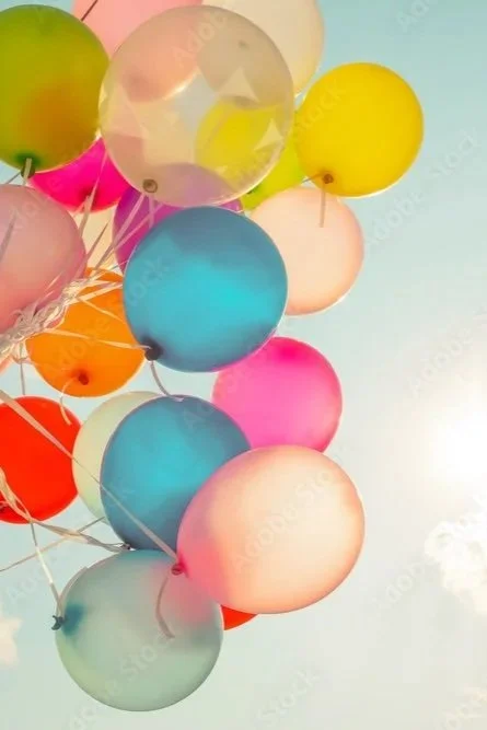Colorful balloons in pink, blue, yellow, green, orange, and clear, floating together against a light background.