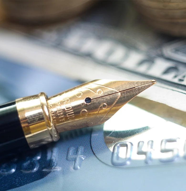 Close-up of a gold fountain pen tip on a cash register or card reader with a dollar bill and coins in the background.