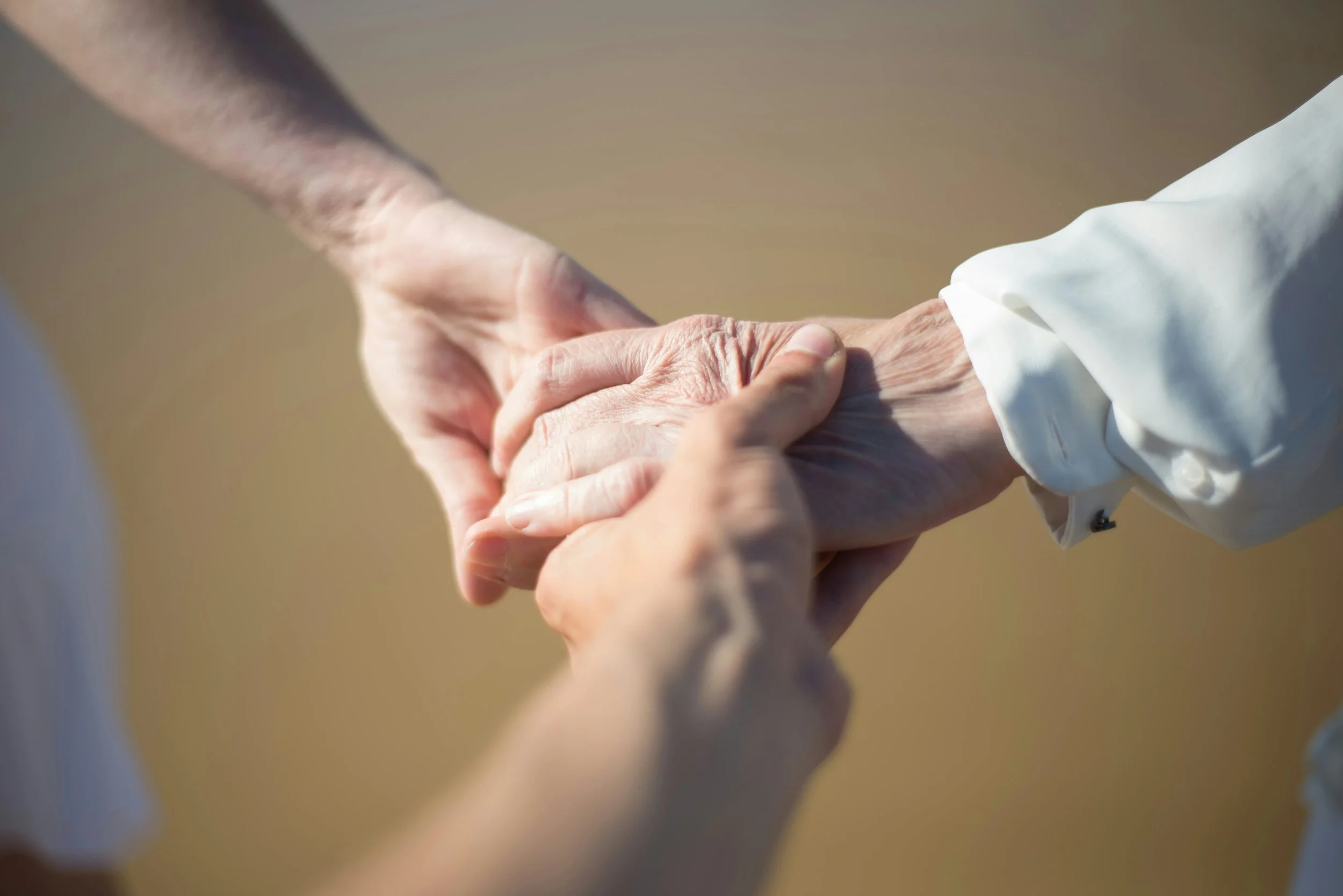 Cropped view of three people holding hands of varying ages, including one older, wrinkled hand.