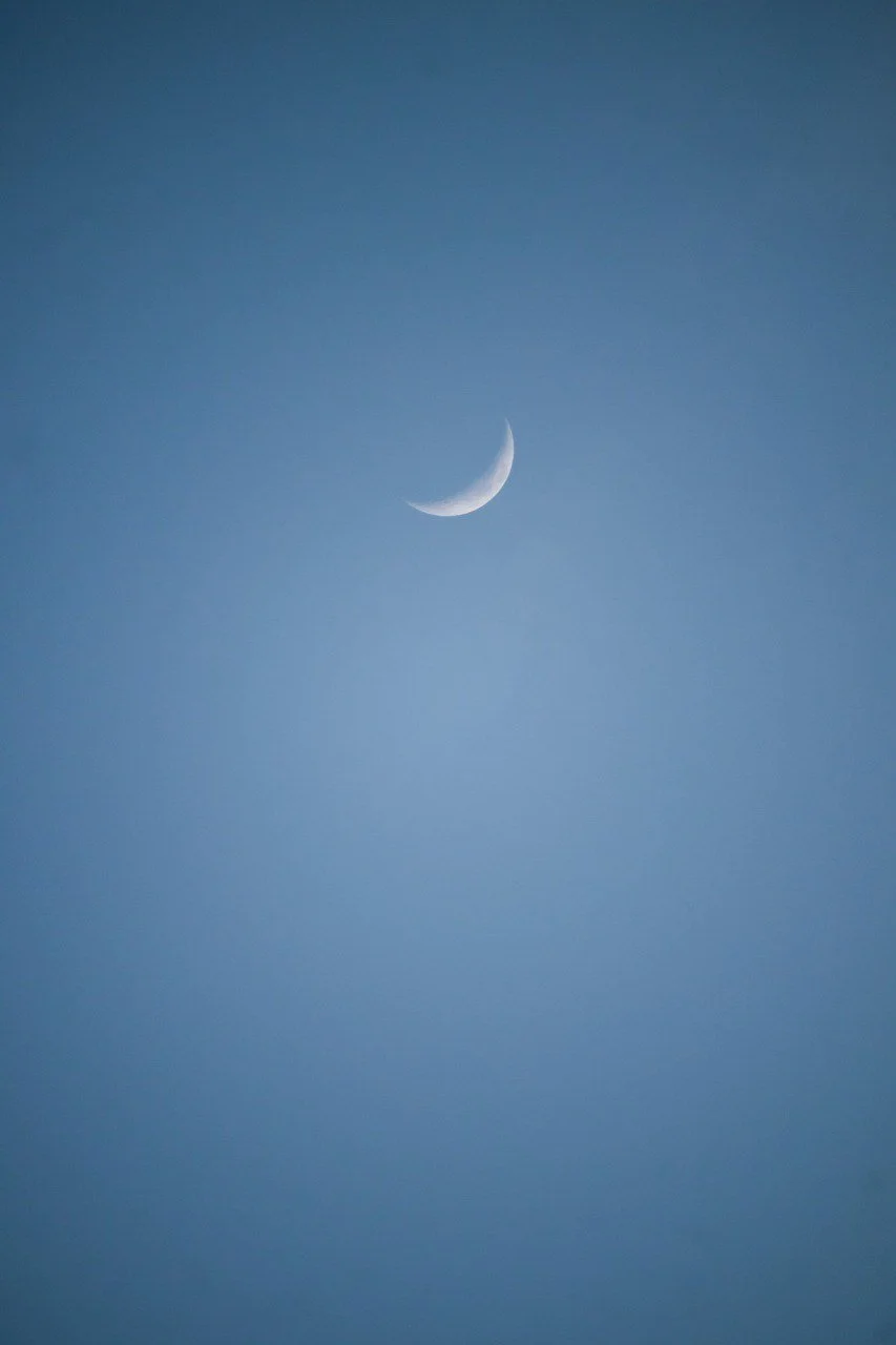 A crescent moon in a clear blue sky. Collective Conscious Counseling.