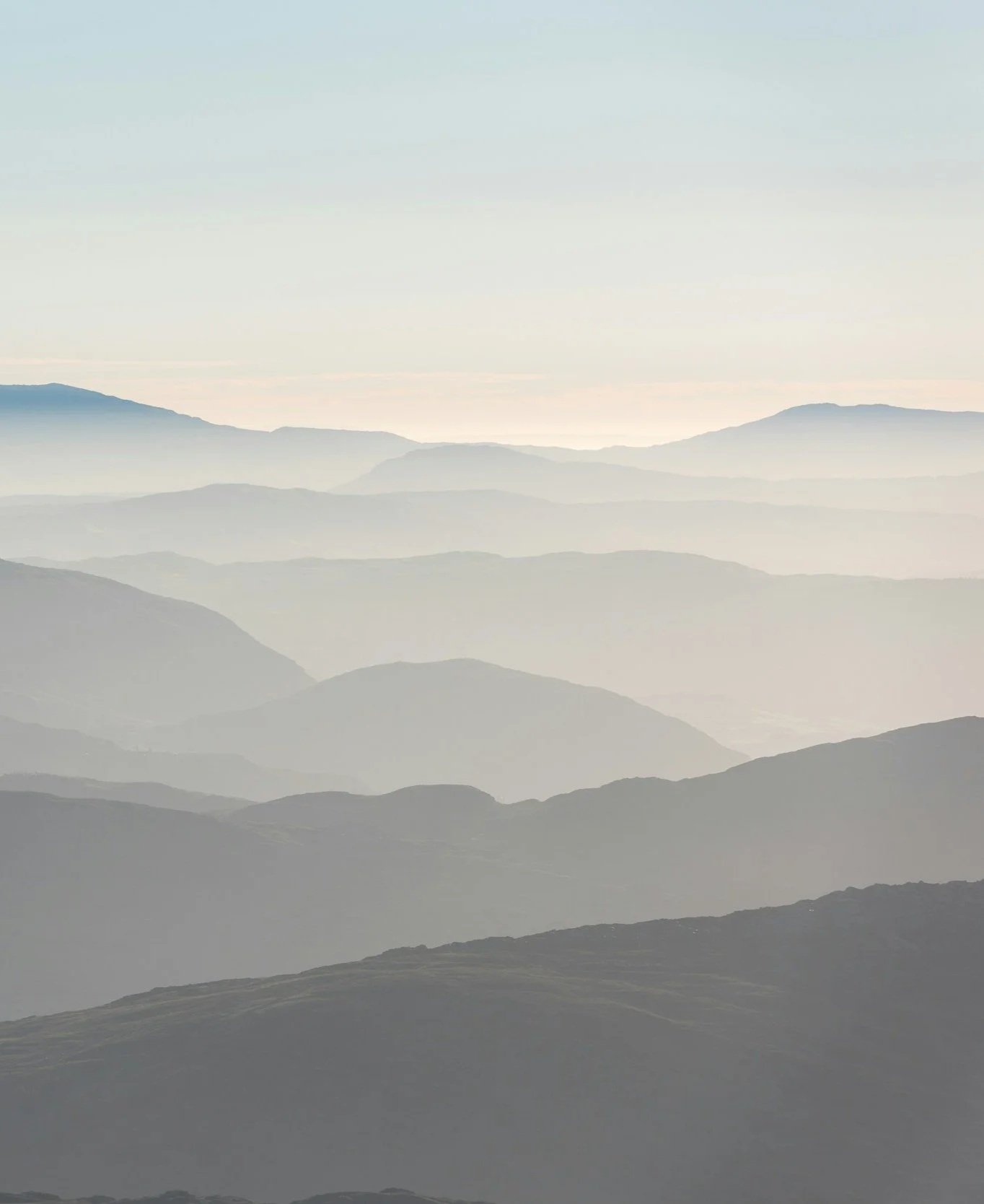 A landscape of multiple mountain ranges fading into the distance with a hazy sky.