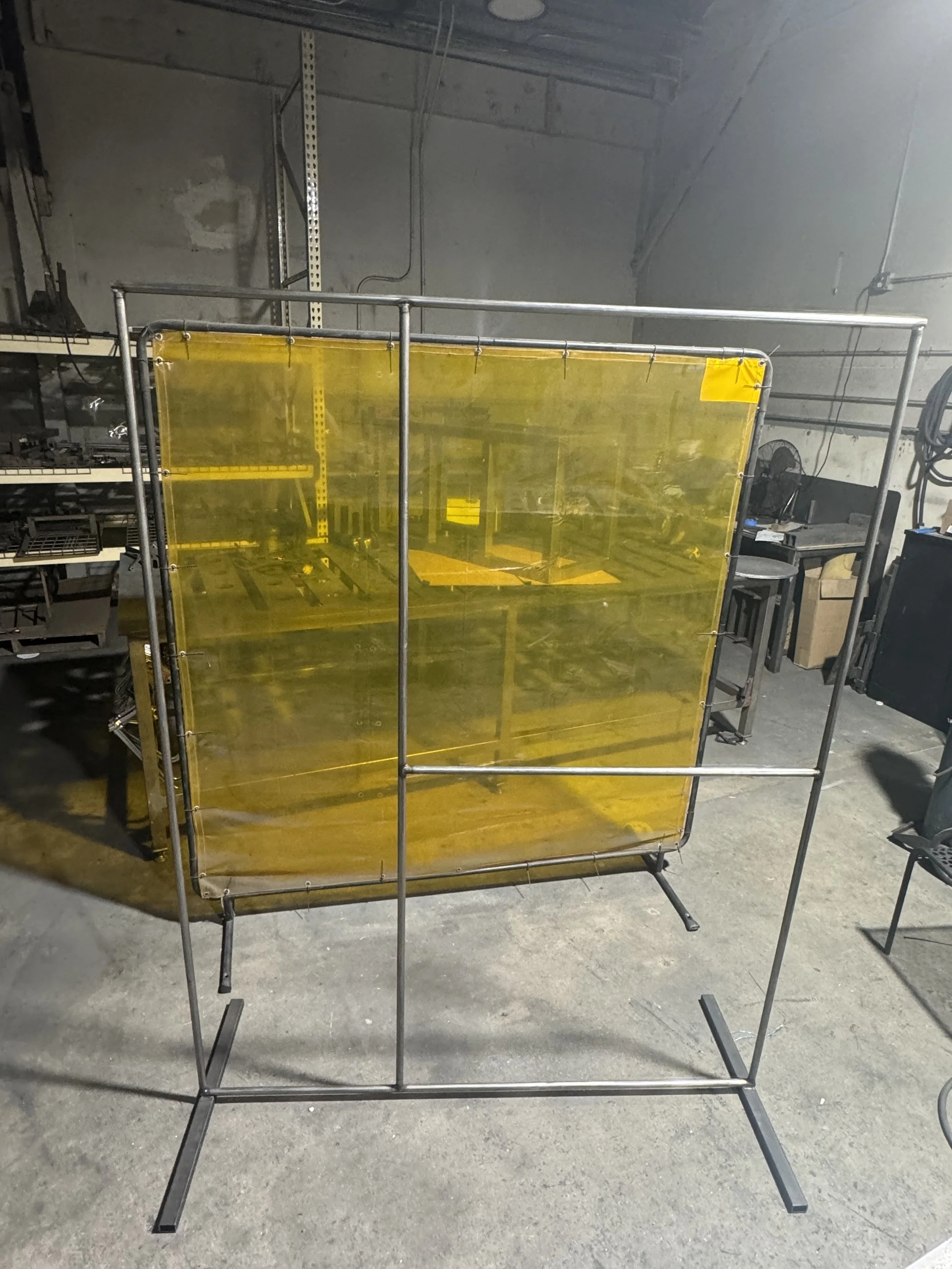 A yellow safety shield attached to a metal frame in an industrial workshop setting.