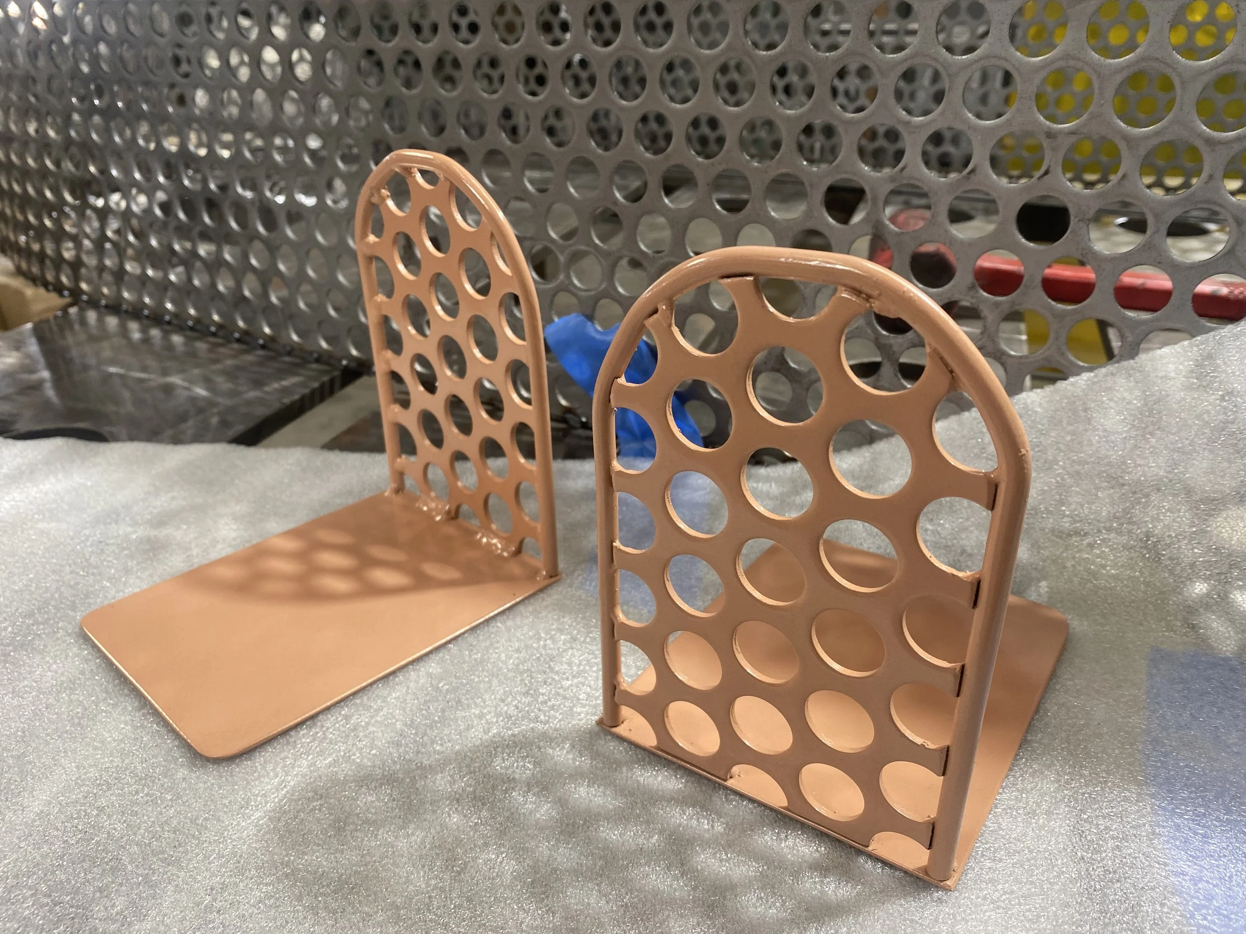 Two peach-colored plastic game pieces with circular holes, resembling shields, placed on a gray fabric surface.