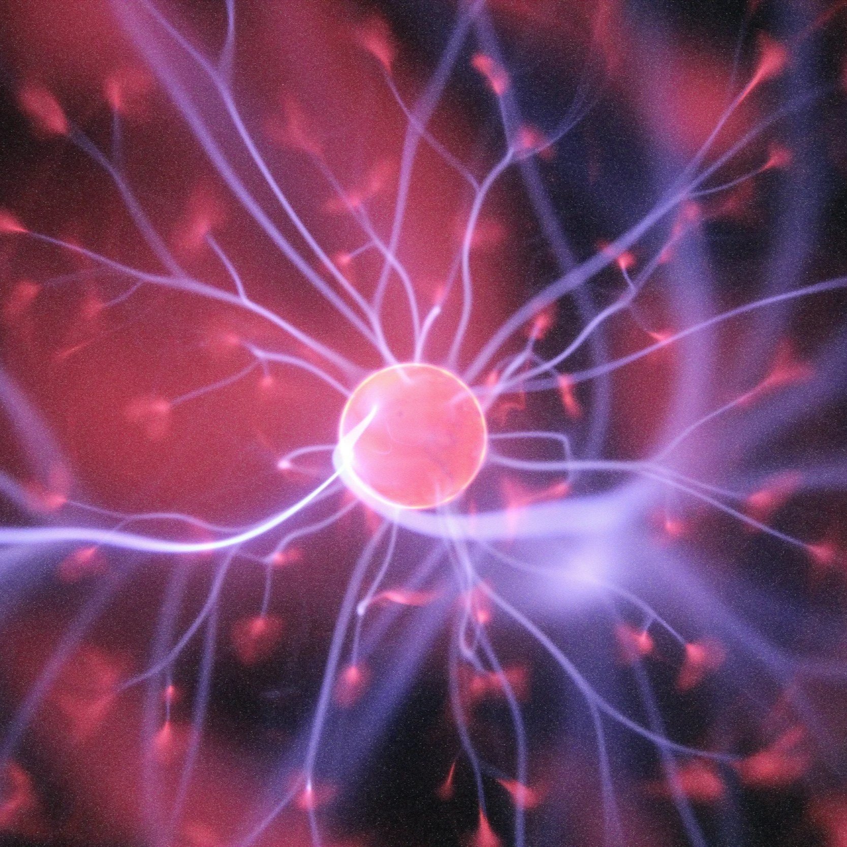 Close-up of a plasma ball with pink and purple electrical filaments emanating from a central glass sphere.
